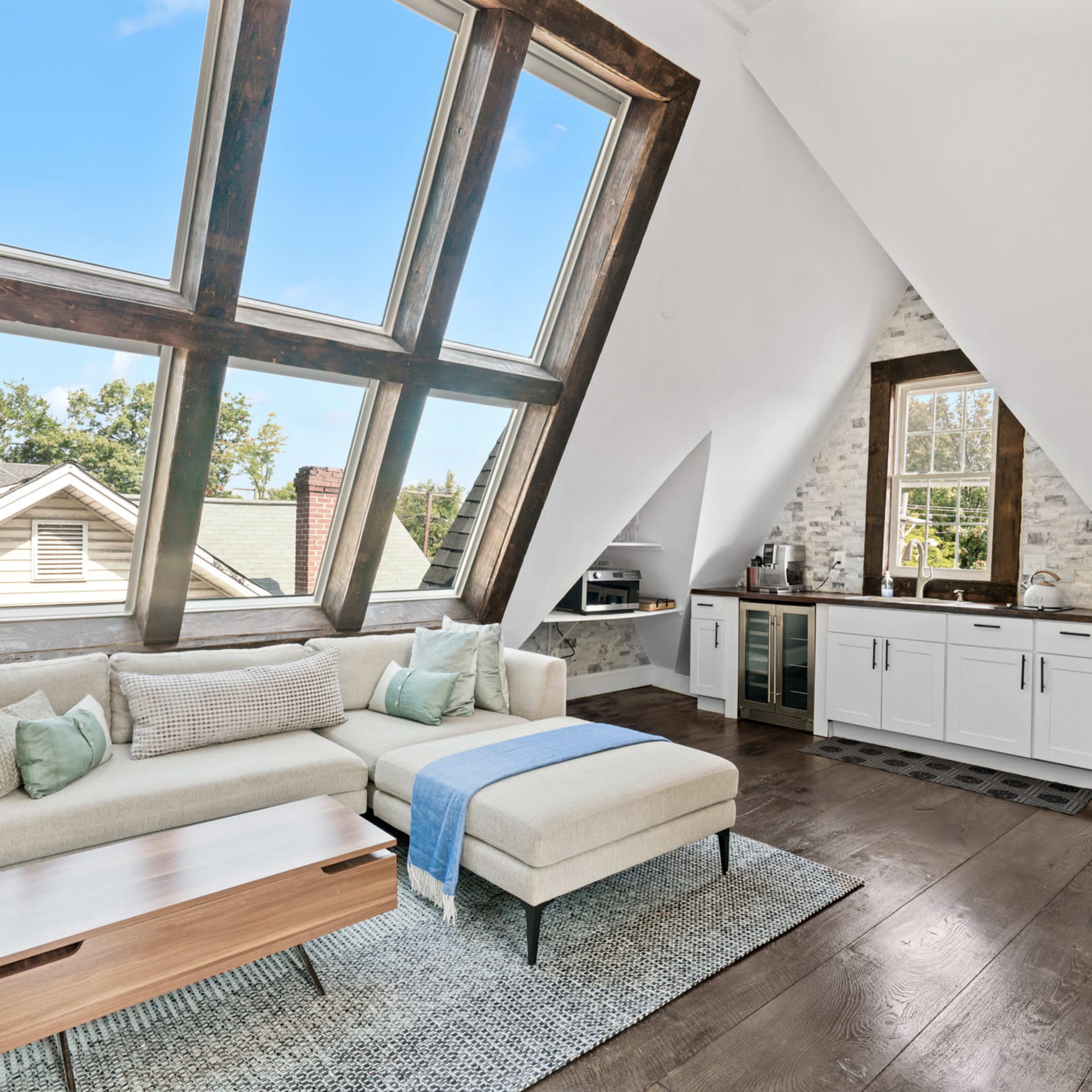 A modern living area with an abstract window design, a sectional sofa, and a kitchenette with wooden accents.