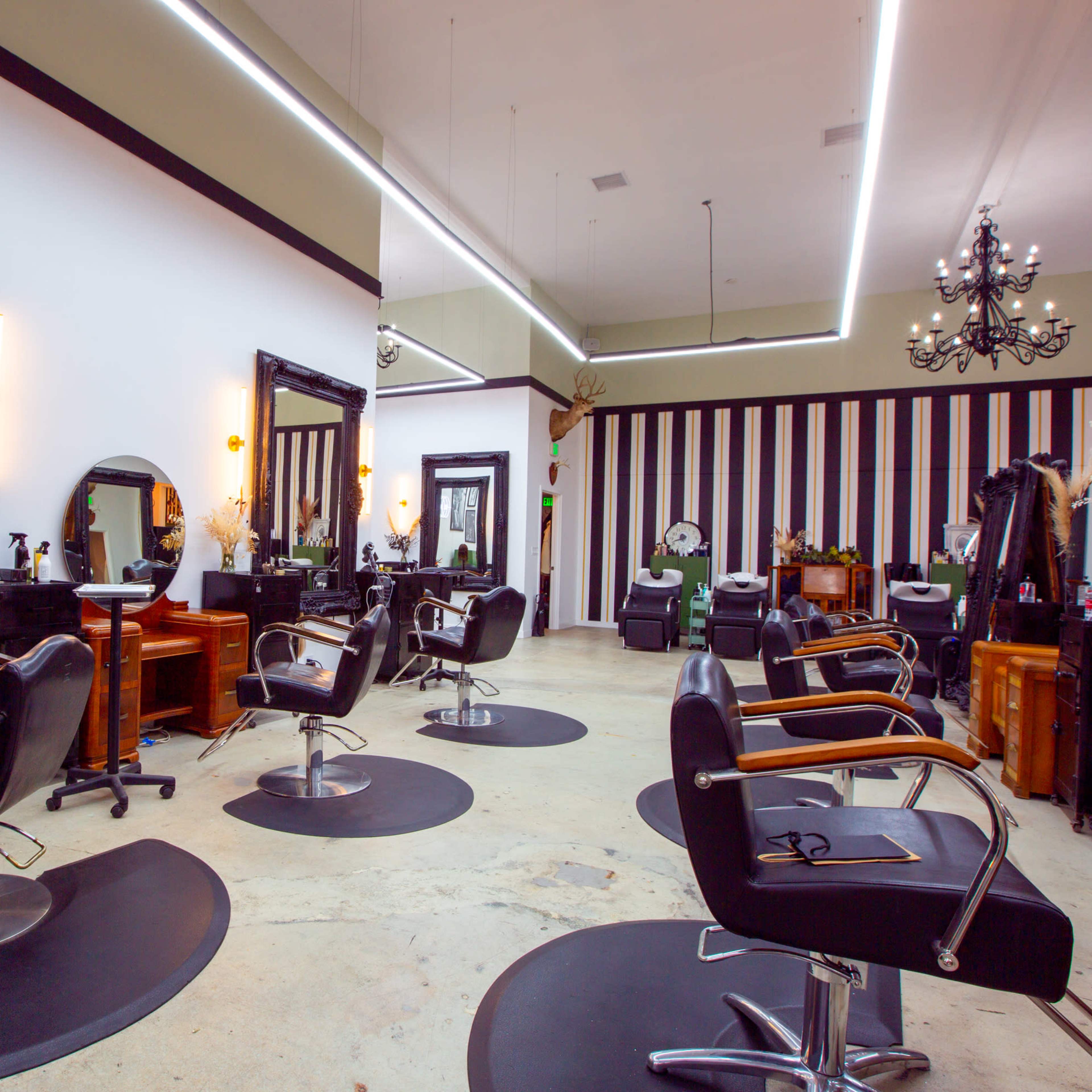 A modern hair salon with black styling chairs, large mirrors, and striped walls.