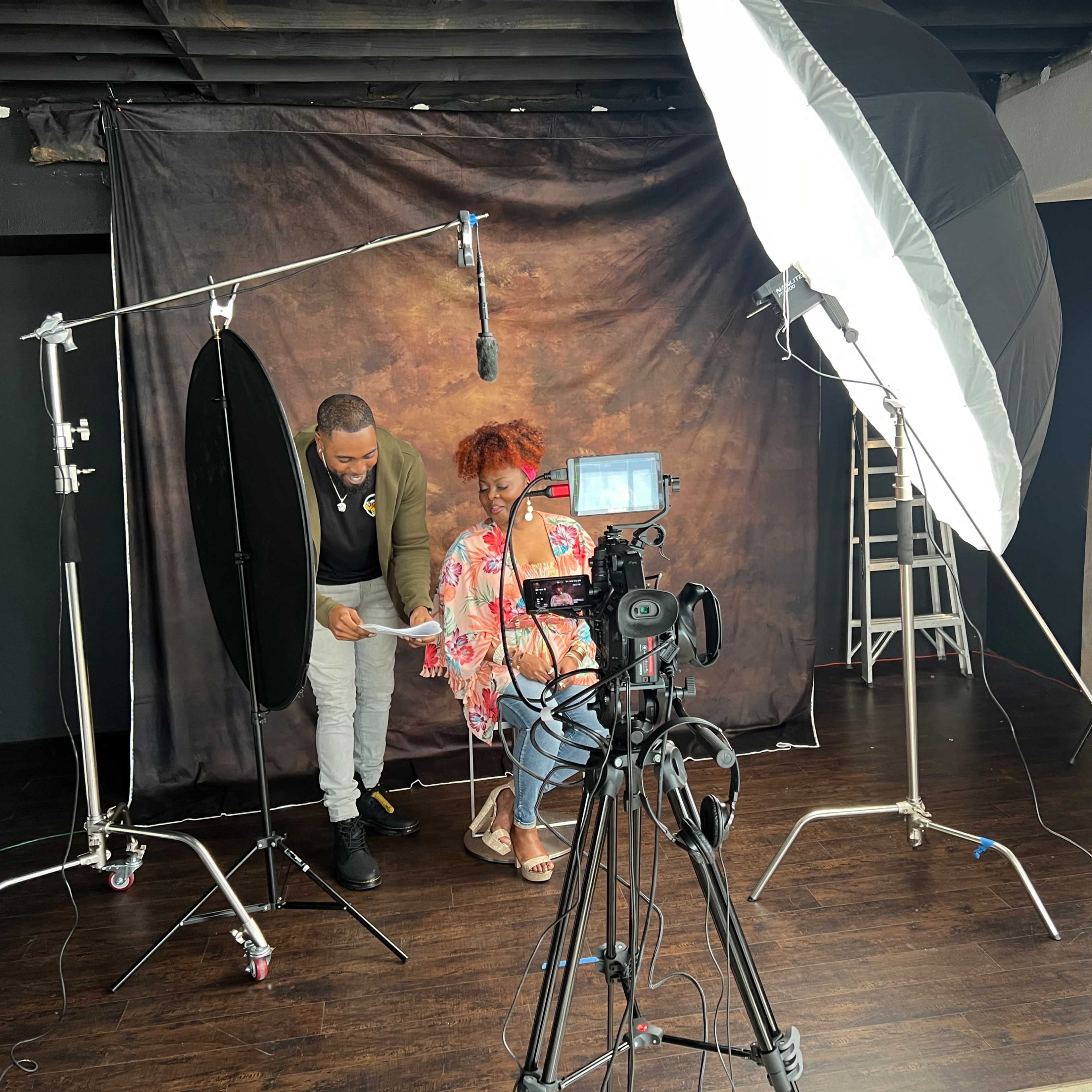 A photographer adjusts lighting equipment while a model poses in a studio setting.