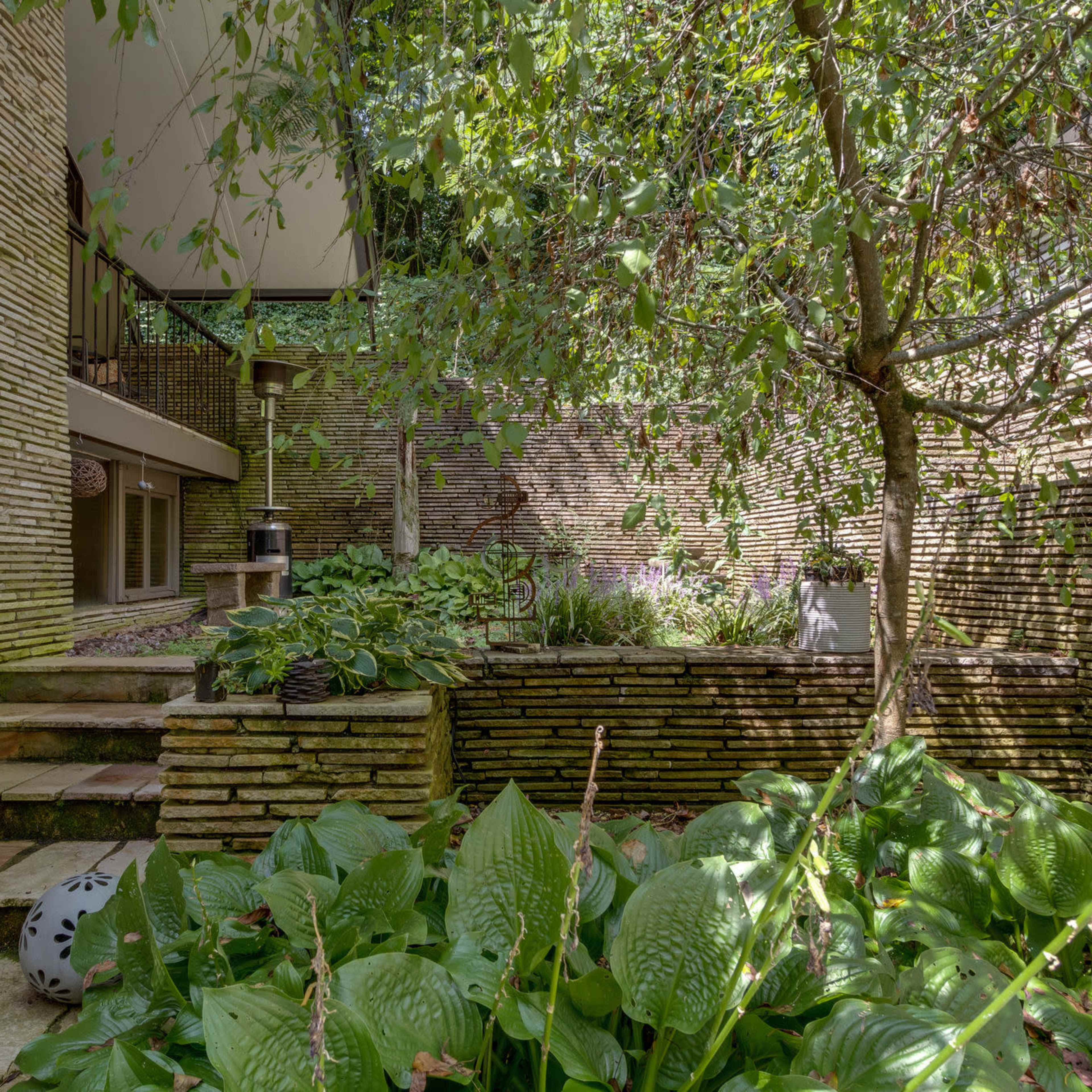 A stone pathway leading up to a mid-century modern building, surrounded by lush greenery and a small tree.