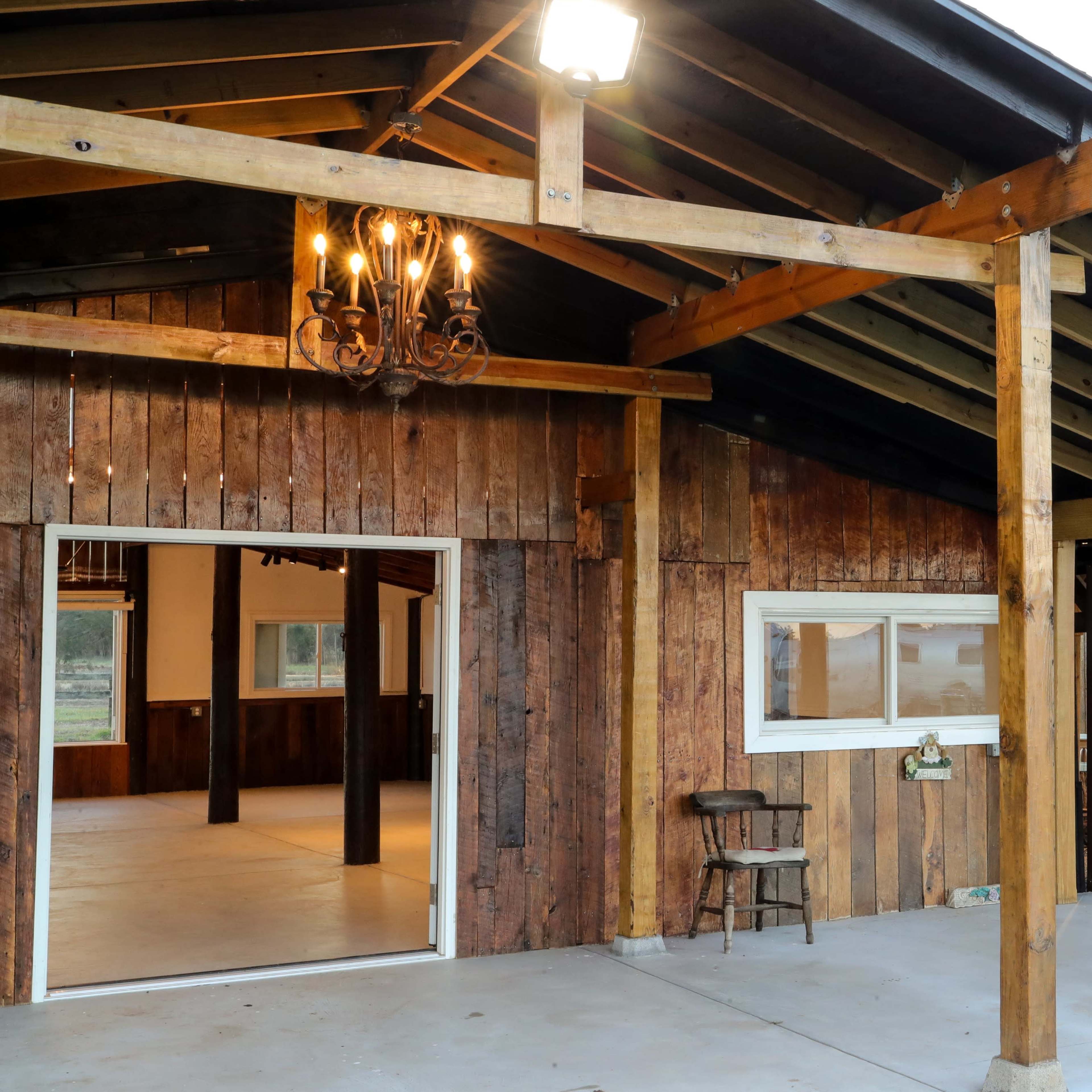 A wooden structure with an open entryway, exposed beams, and a chandelier, leading to a spacious interior.