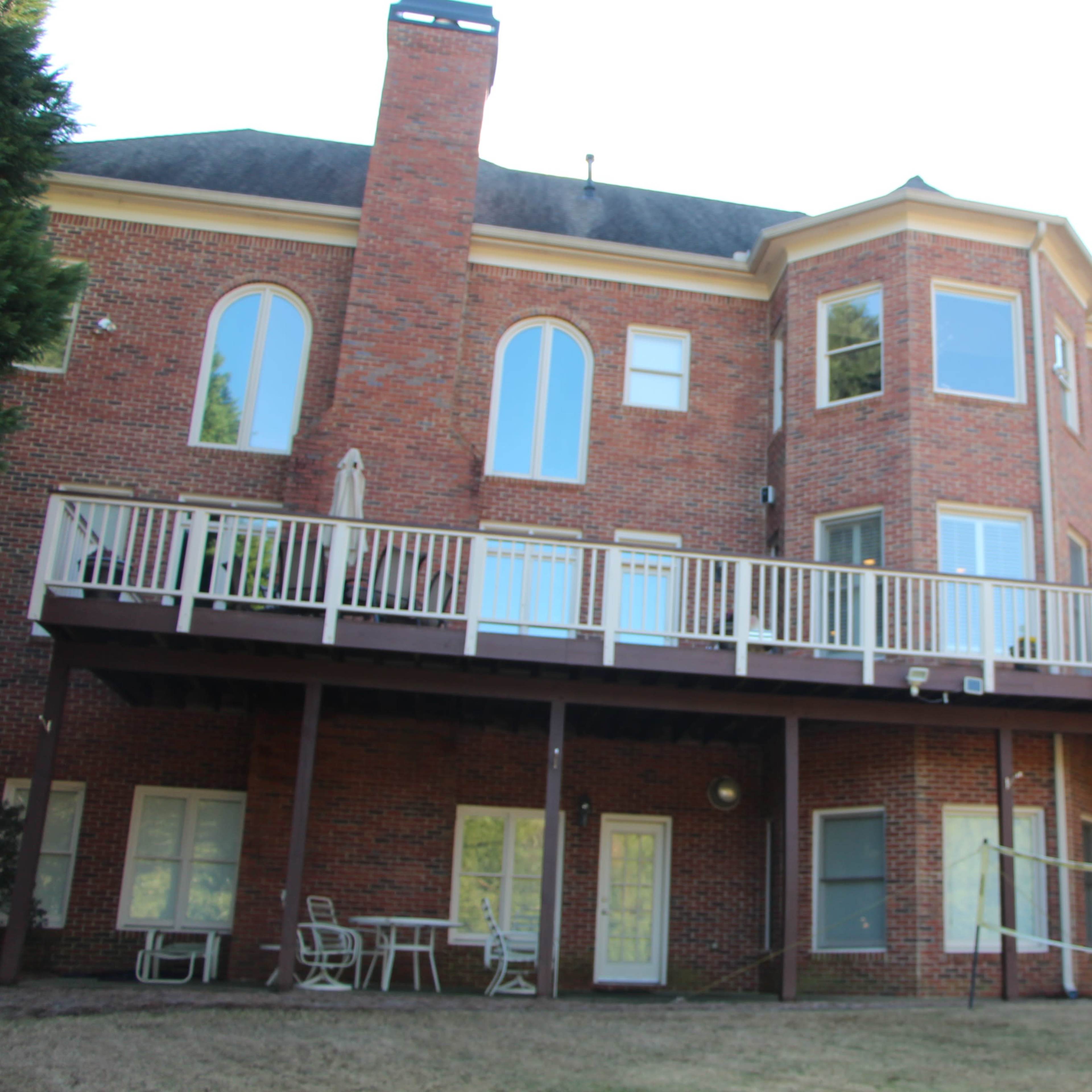 A two-story brick house with large windows and a wooden deck overlooking a backyard.
