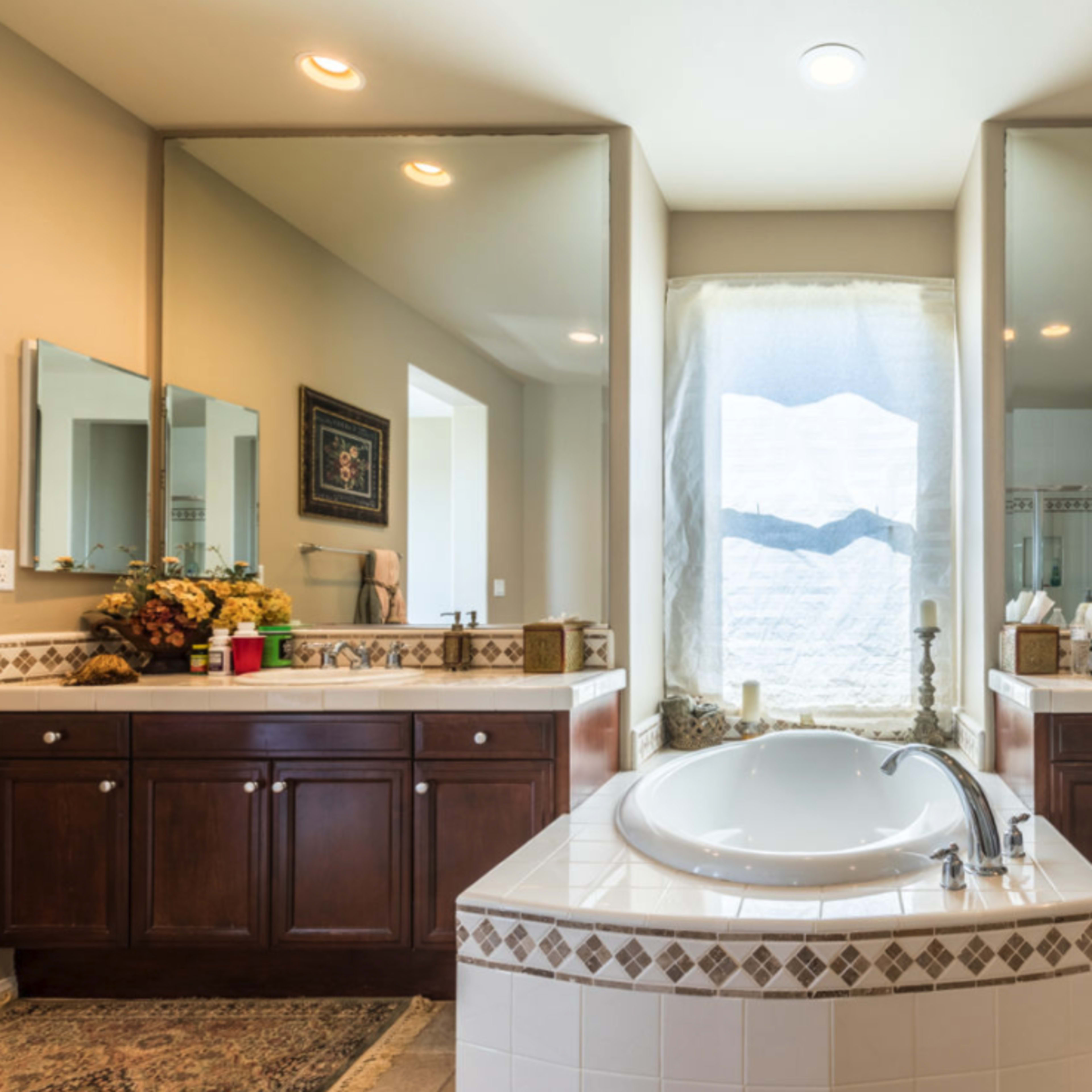 A spacious bathroom featuring dual vanities, a large soaking tub, and a window dressed with a sheer curtain.