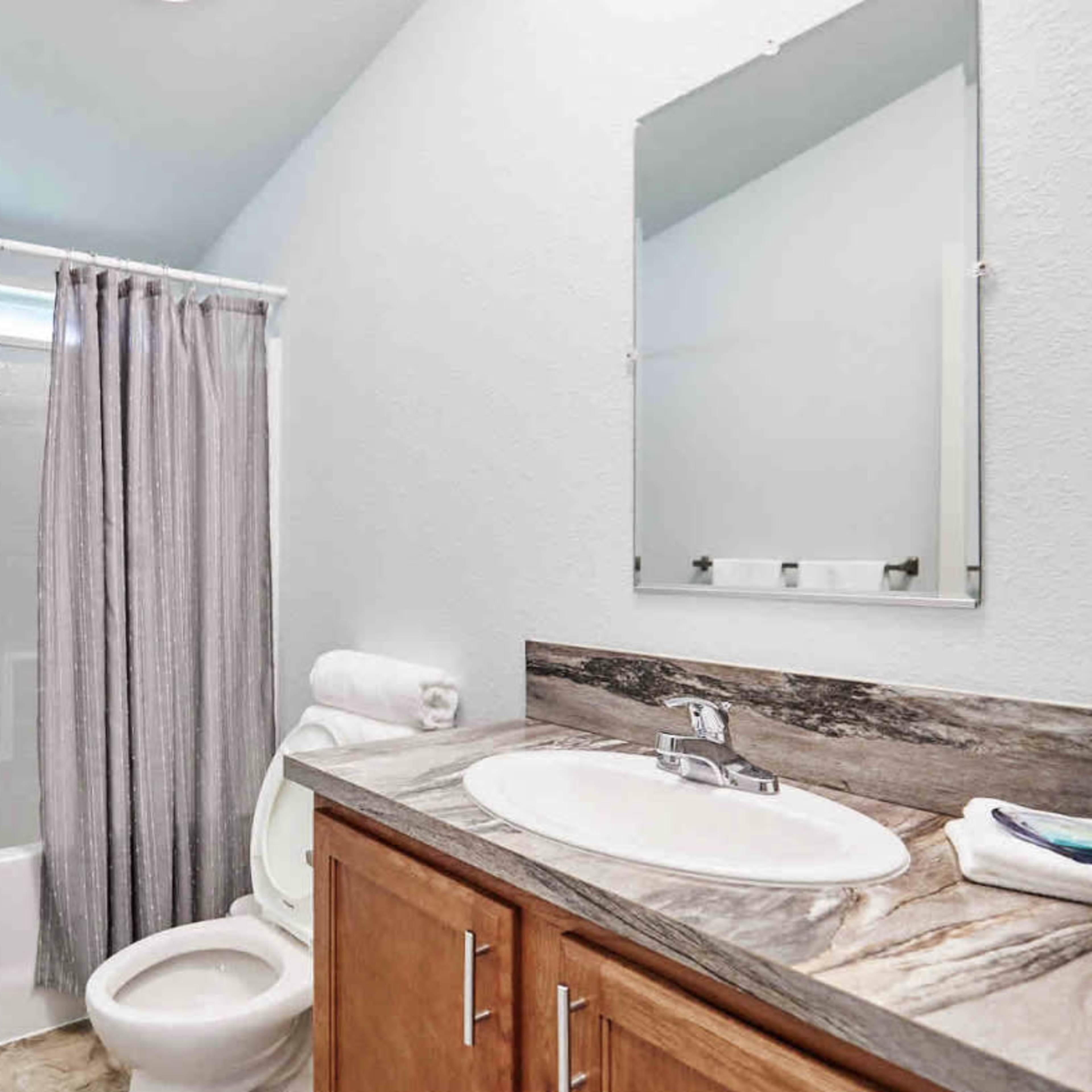 The bathroom features a shower with a curtain, a toilet, a sink with a countertop, and light-colored walls.