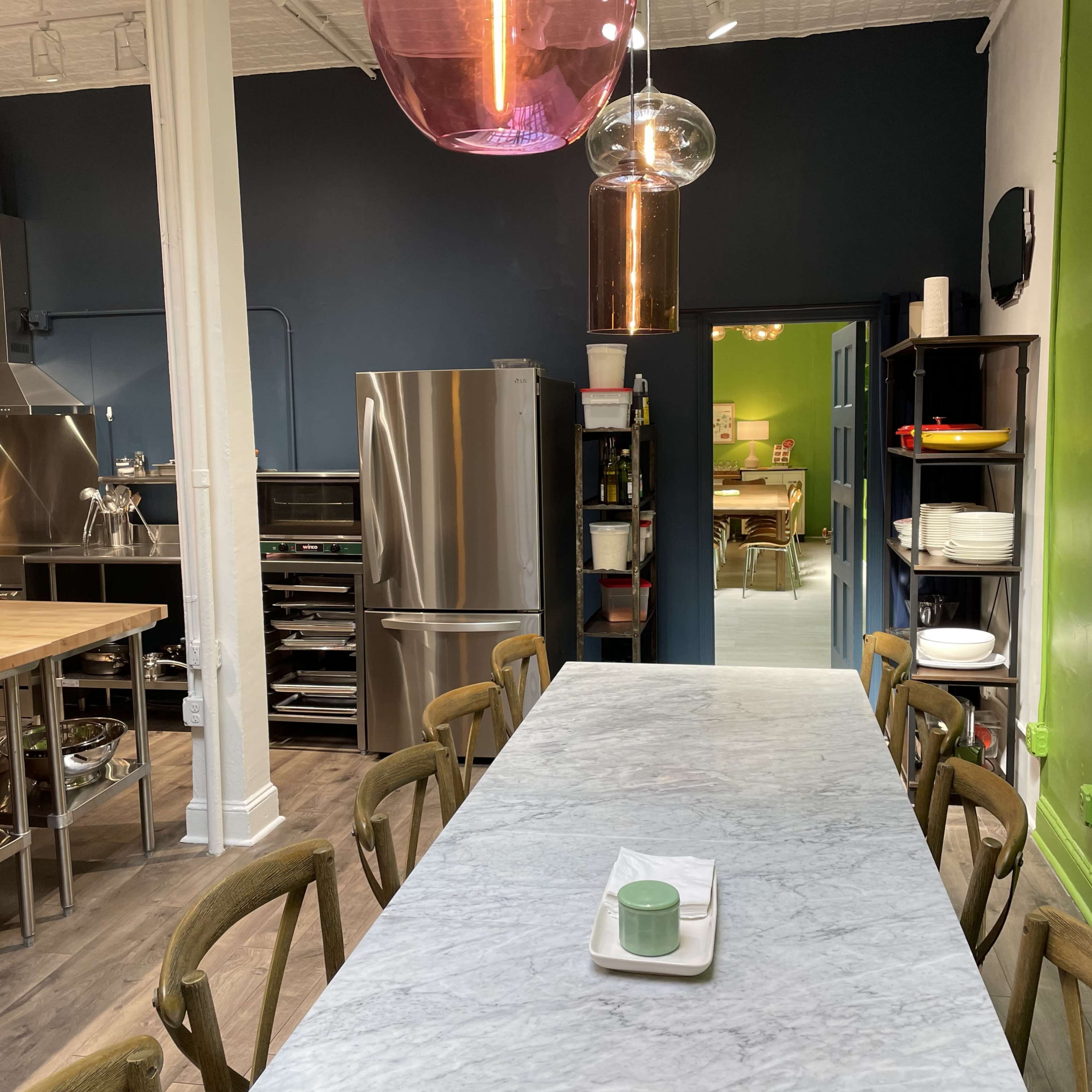 A spacious kitchen features a long marble table, stainless steel appliances, and vibrant green and blue walls.