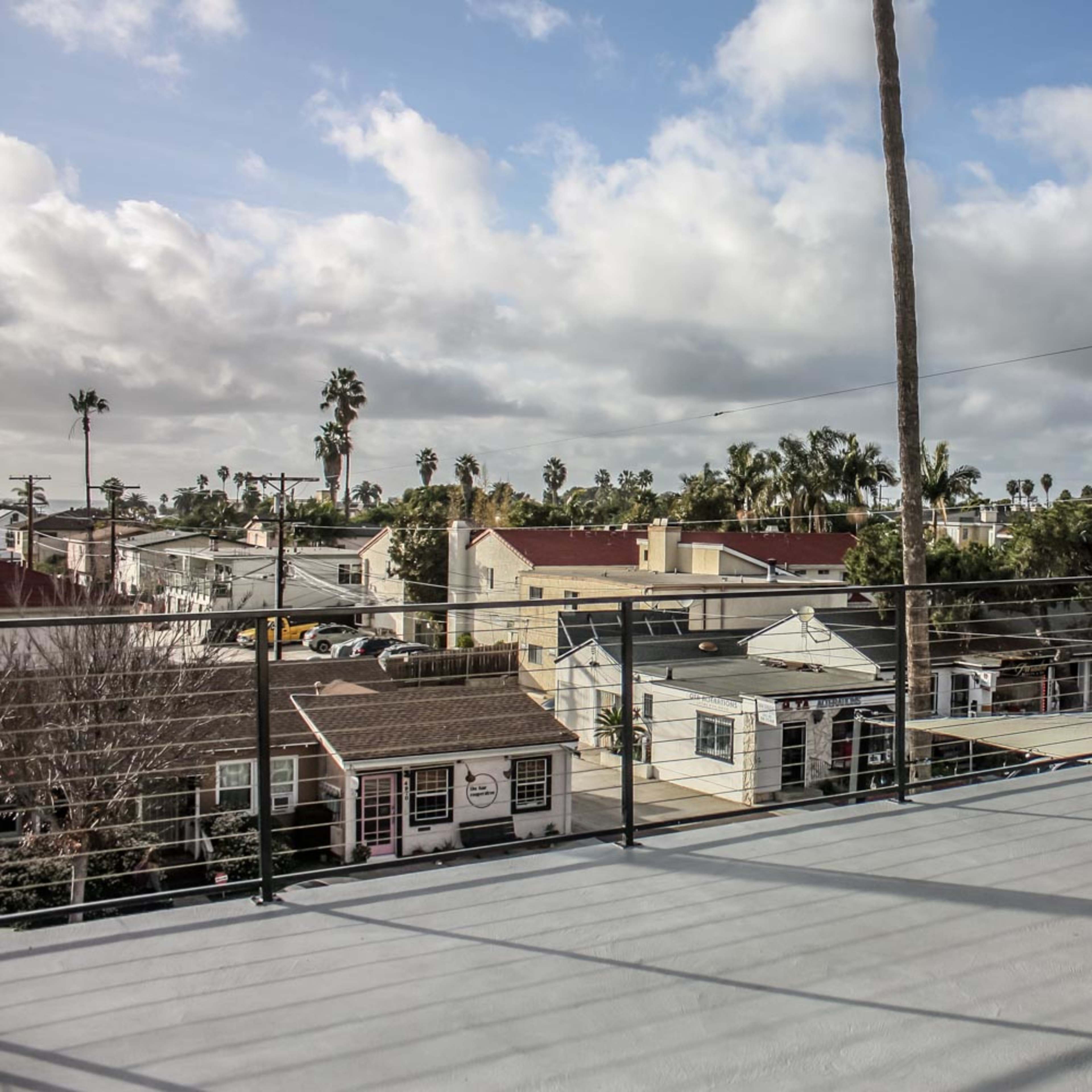 A rooftop deck overlooking a neighborhood with houses, palm trees, and cloudy skies in the background.