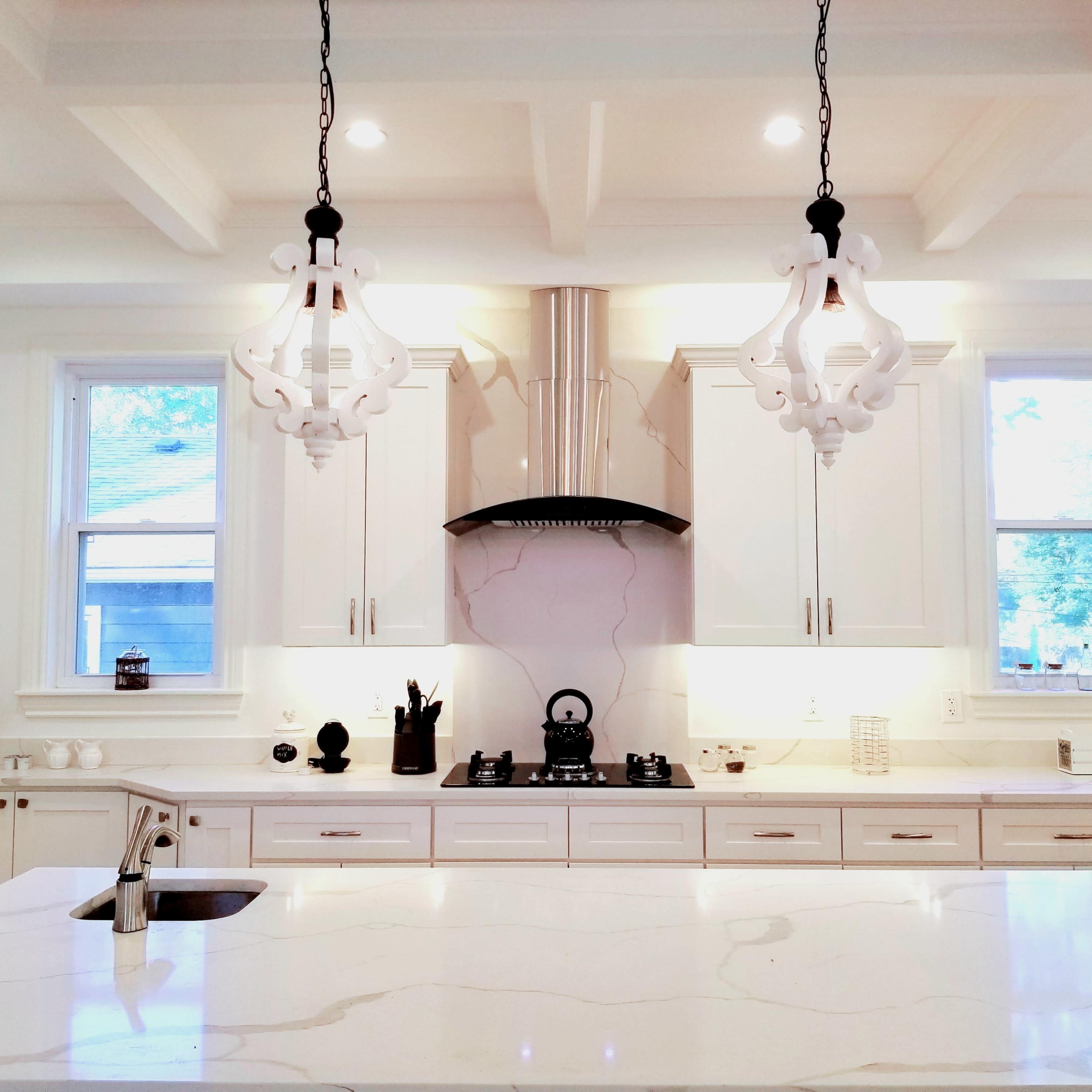 A modern kitchen features white cabinetry, a large marble island, and two pendant lights hanging above.