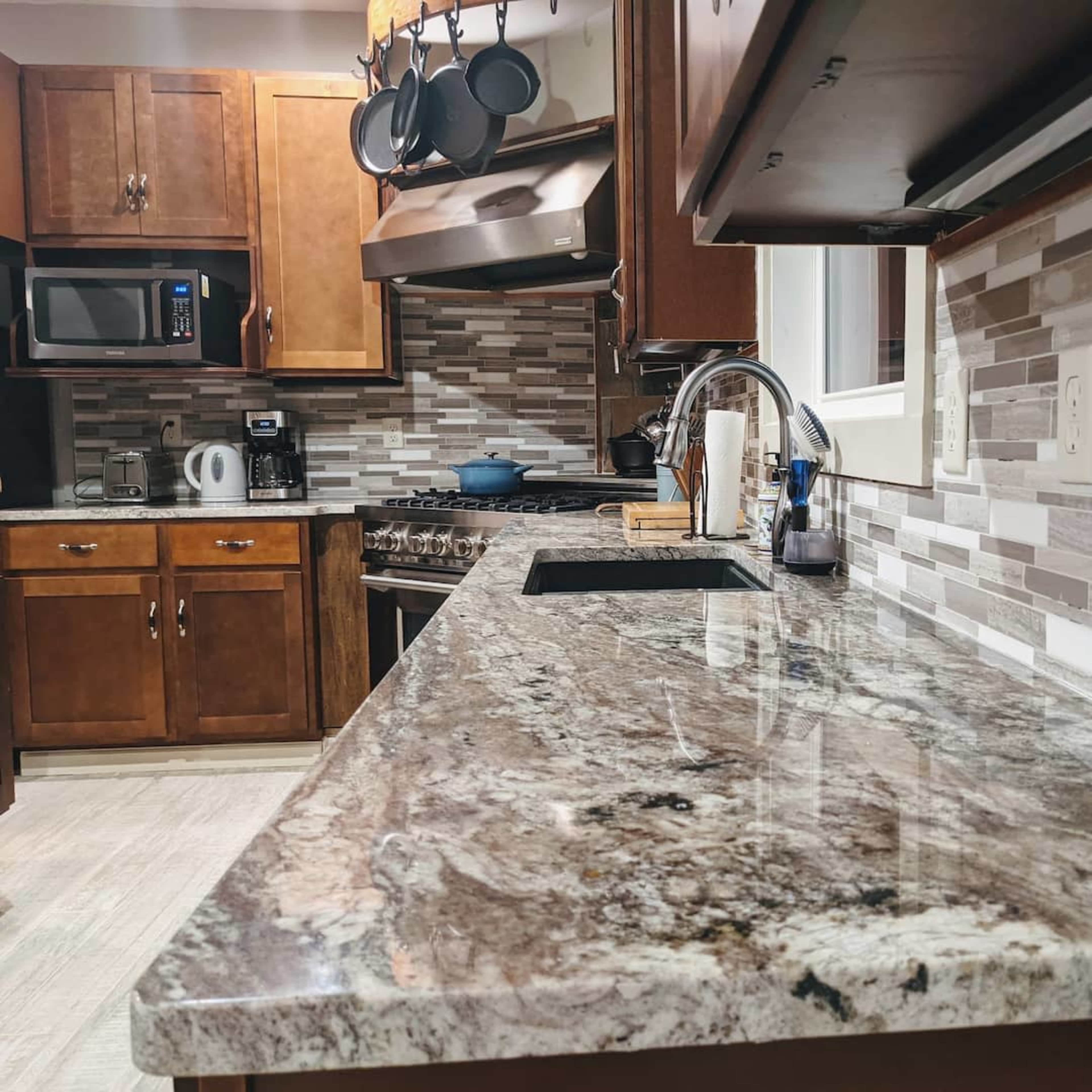 A modern kitchen with wooden cabinets, a granite countertop, and a backsplash made of light-colored tiles.