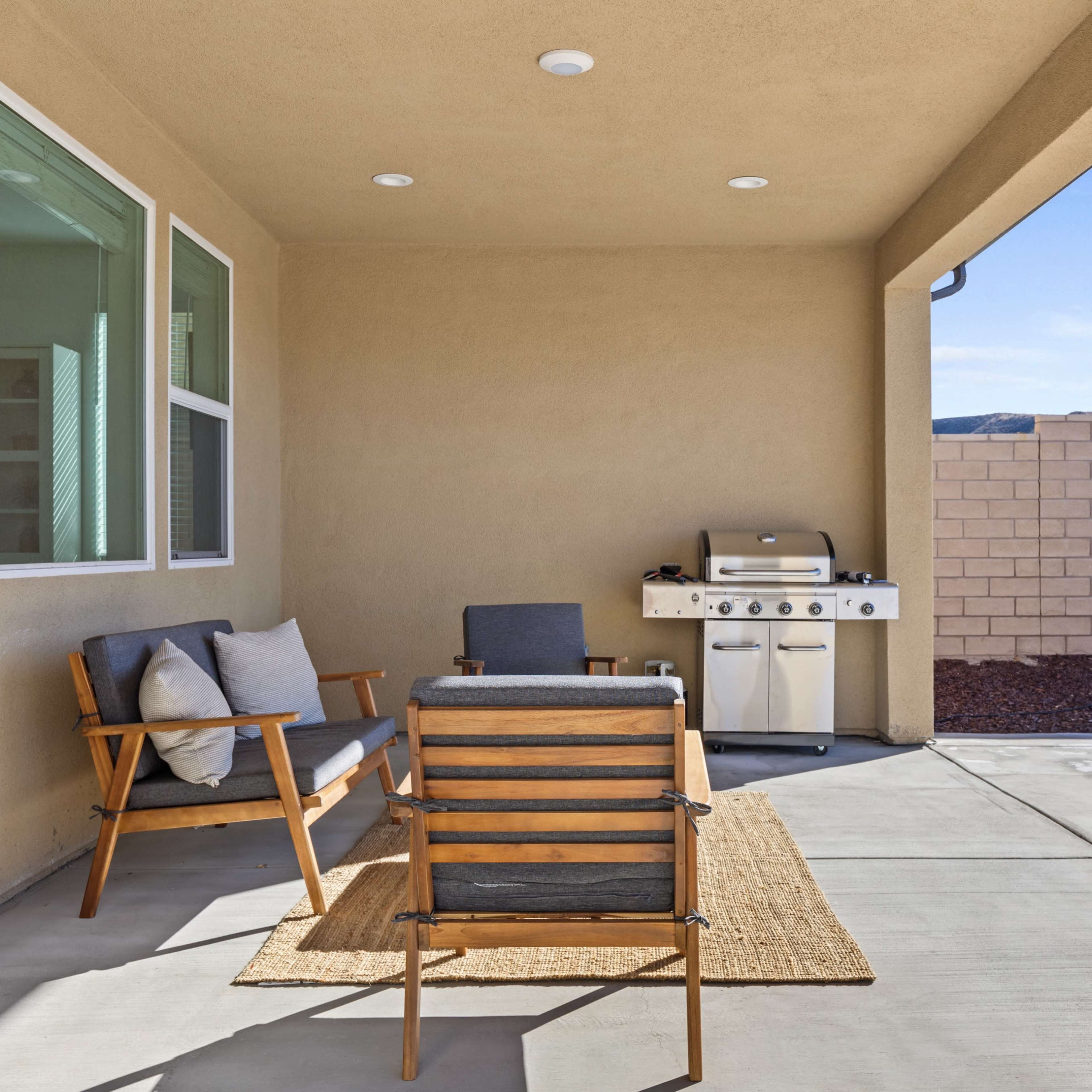 A patio area with two wooden chairs, a small side table, and a barbecue grill against a wall.