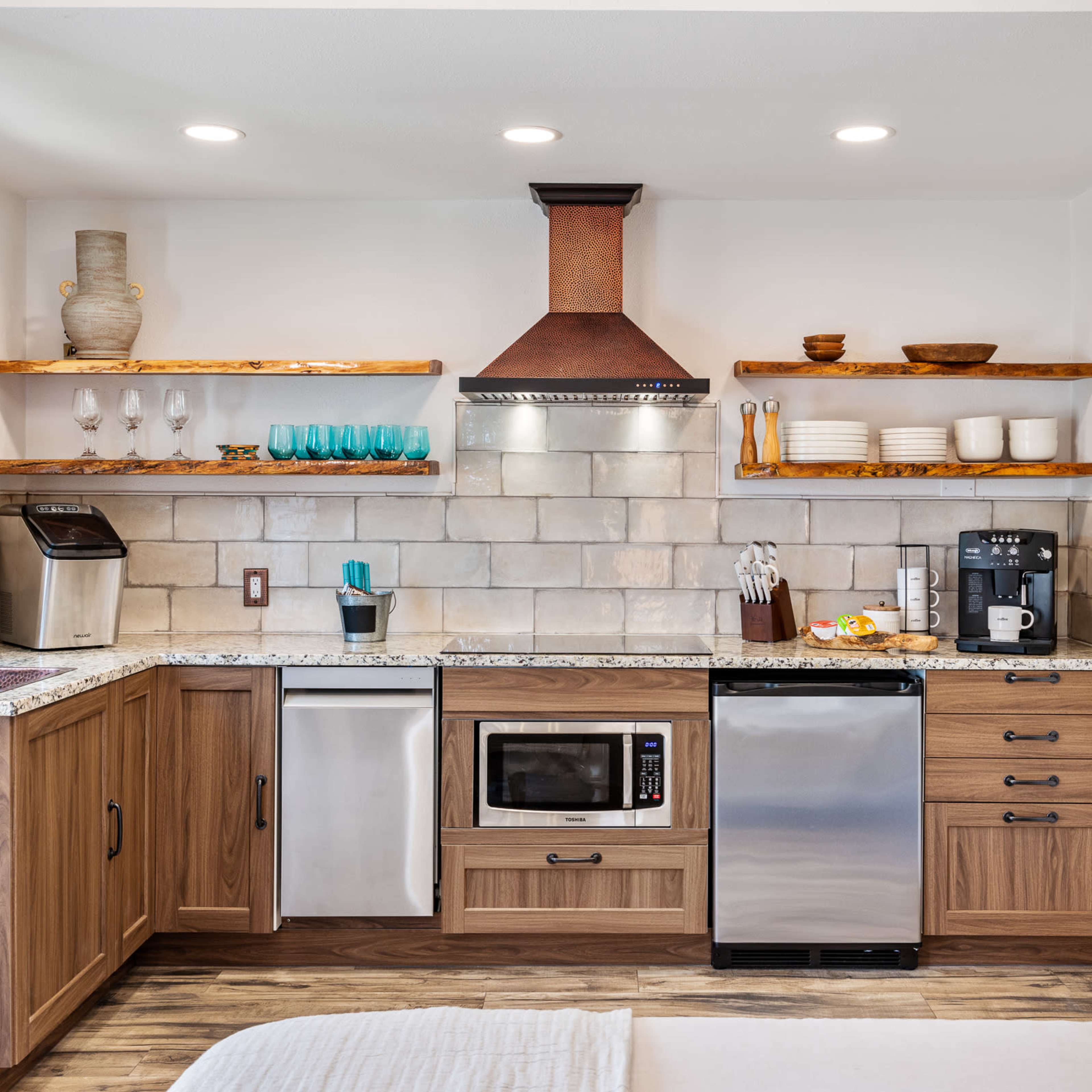 A modern kitchen featuring wooden cabinetry, granite countertops, stainless steel appliances, and open shelving with dishware.