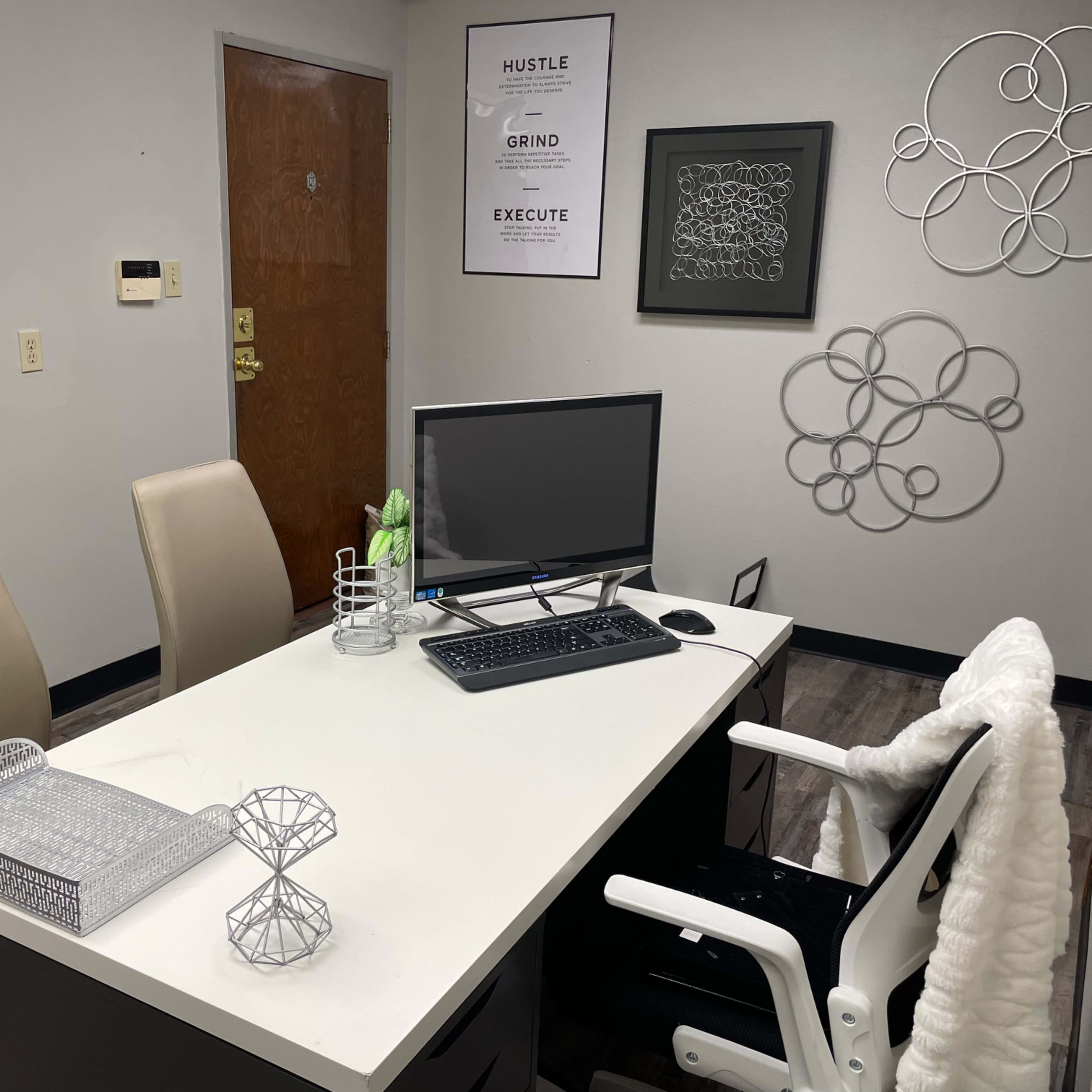 A small office with a desk, a computer, two chairs, and wall decorations.