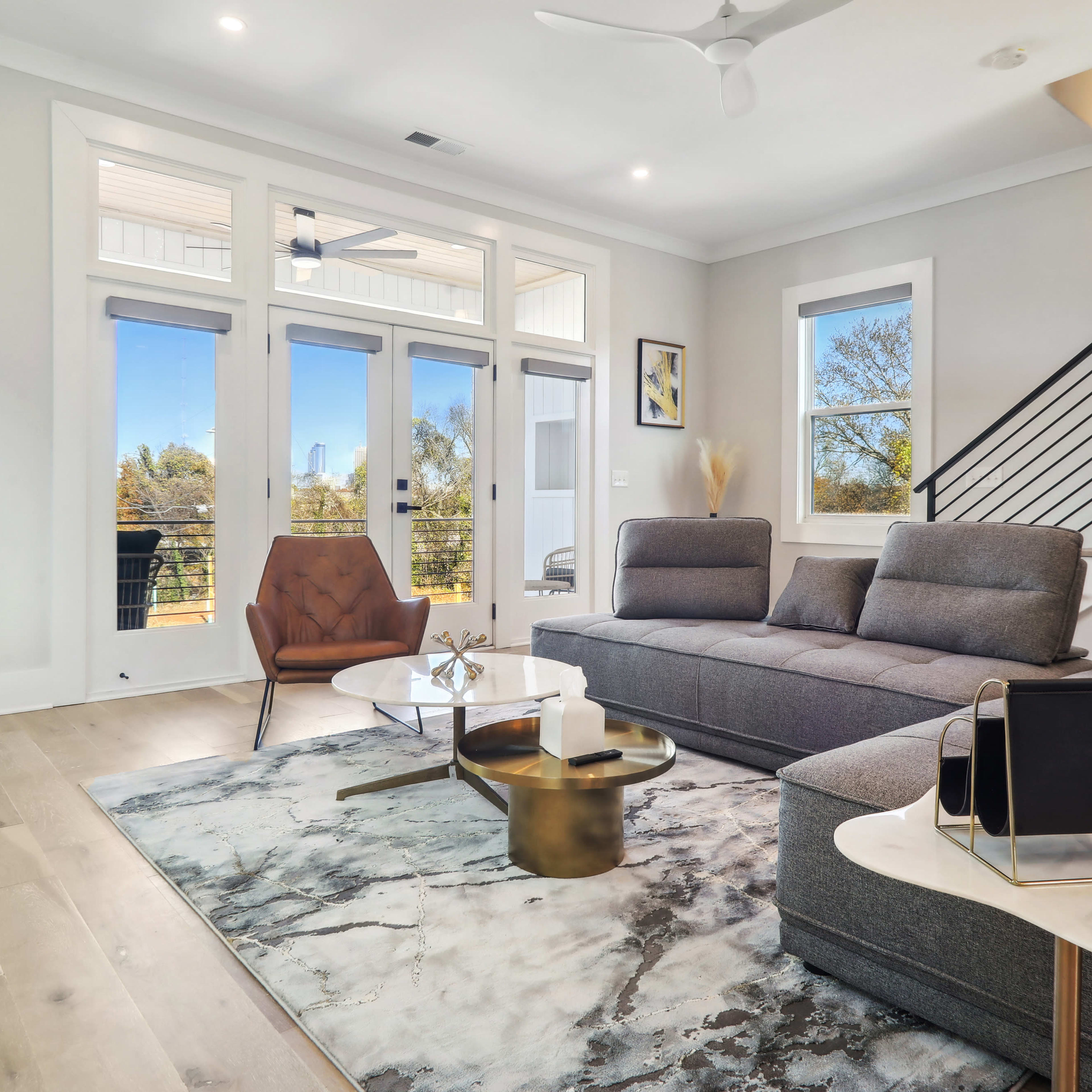 The living room features a modern sofa arrangement, a coffee table, and large windows that provide a view of the exterior.