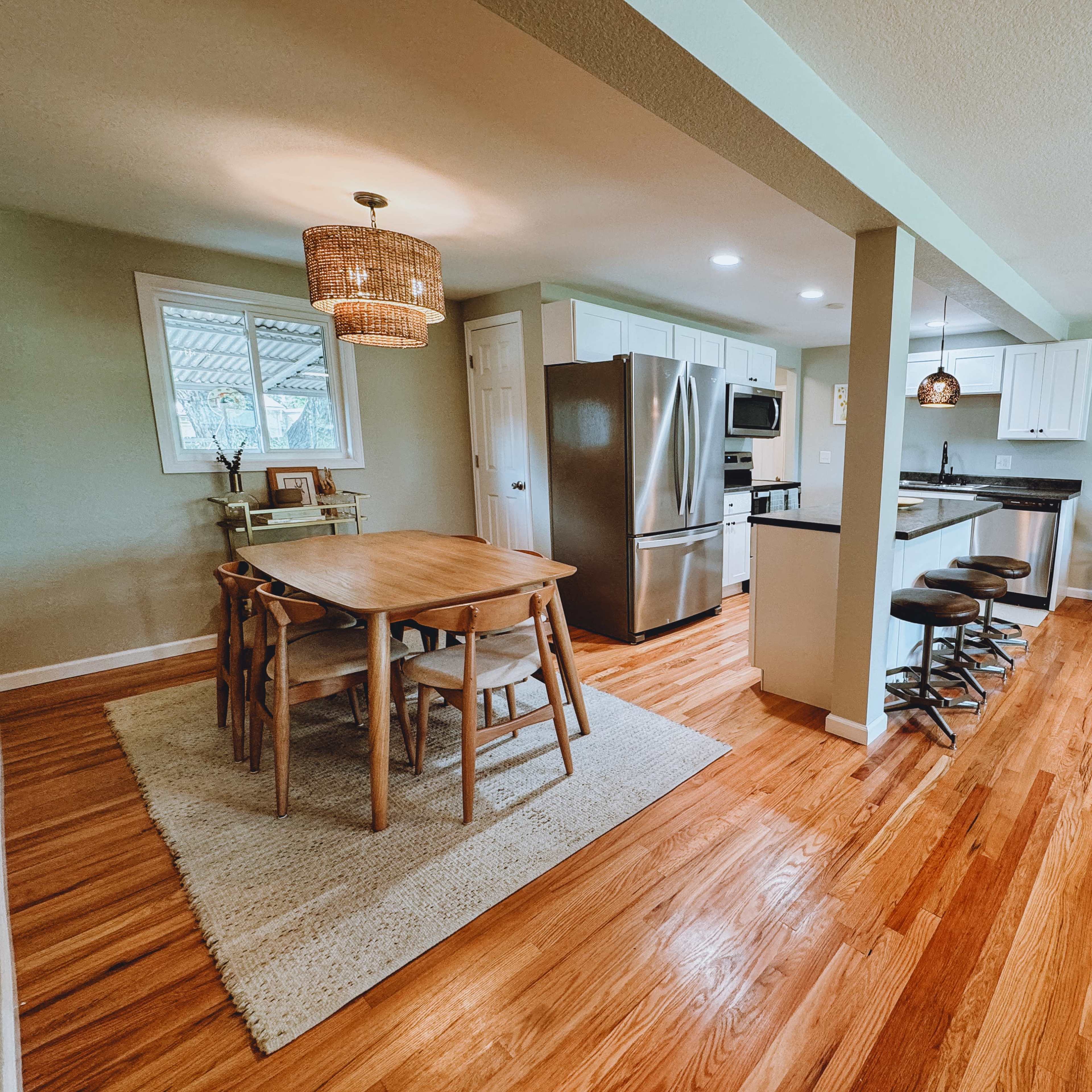 A spacious dining area with a wooden table and chairs, leading into a modern kitchen with stainless steel appliances and a bar seating area.