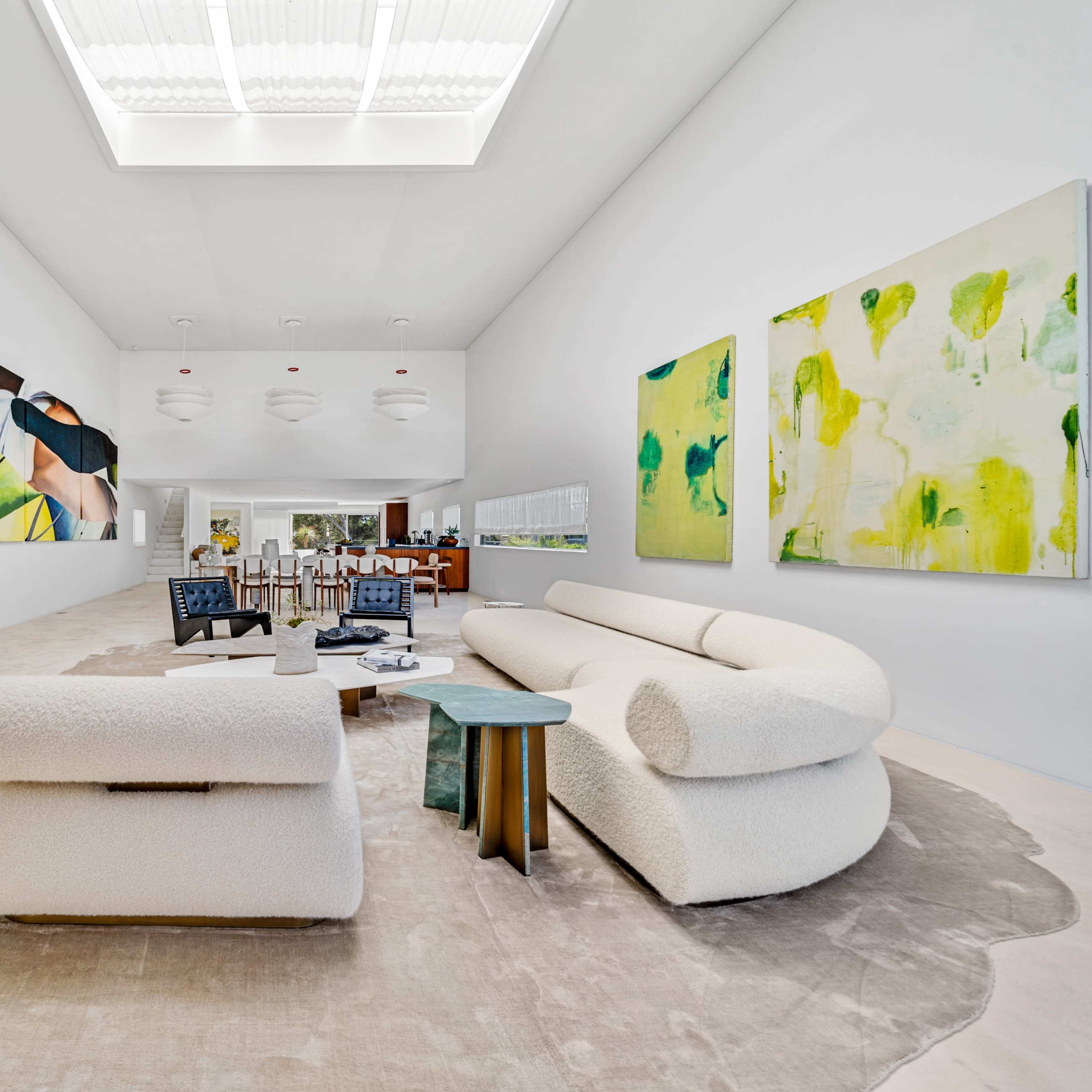 A spacious, modern interior featuring large abstract paintings on the walls, a plush beige sofa, and a central coffee table on a light rug.