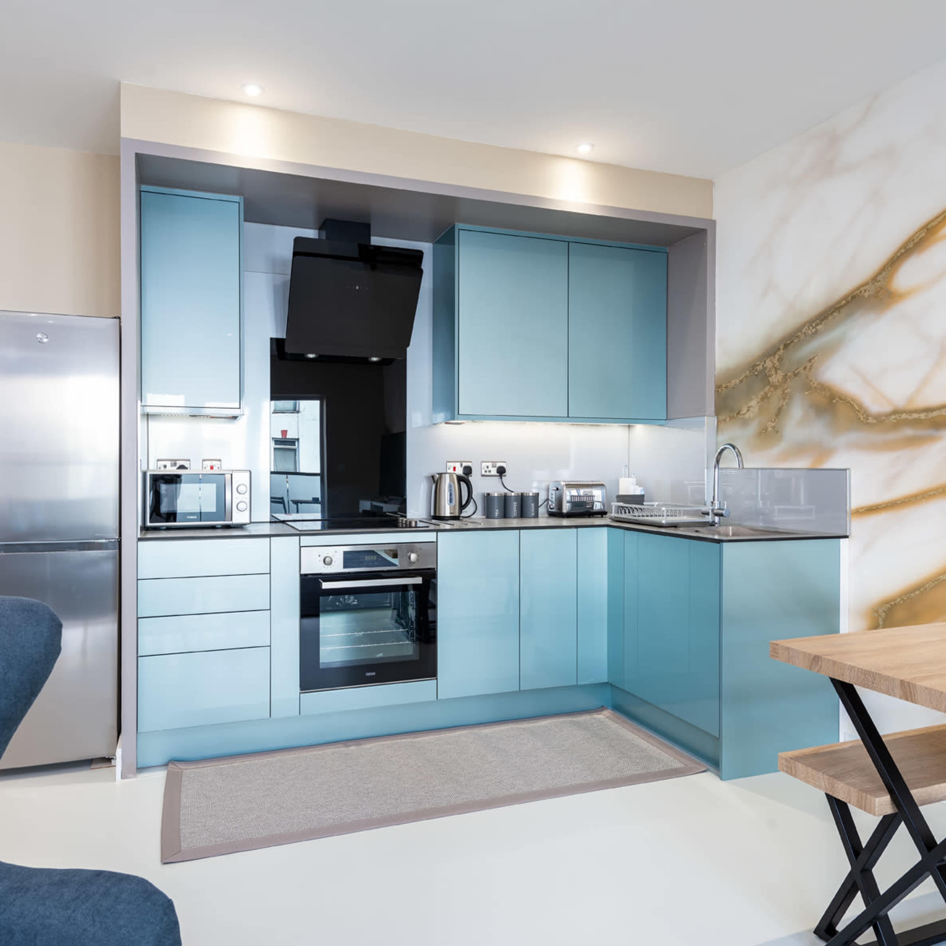 A modern kitchen with blue cabinetry, stainless steel appliances, and a wooden dining table.
