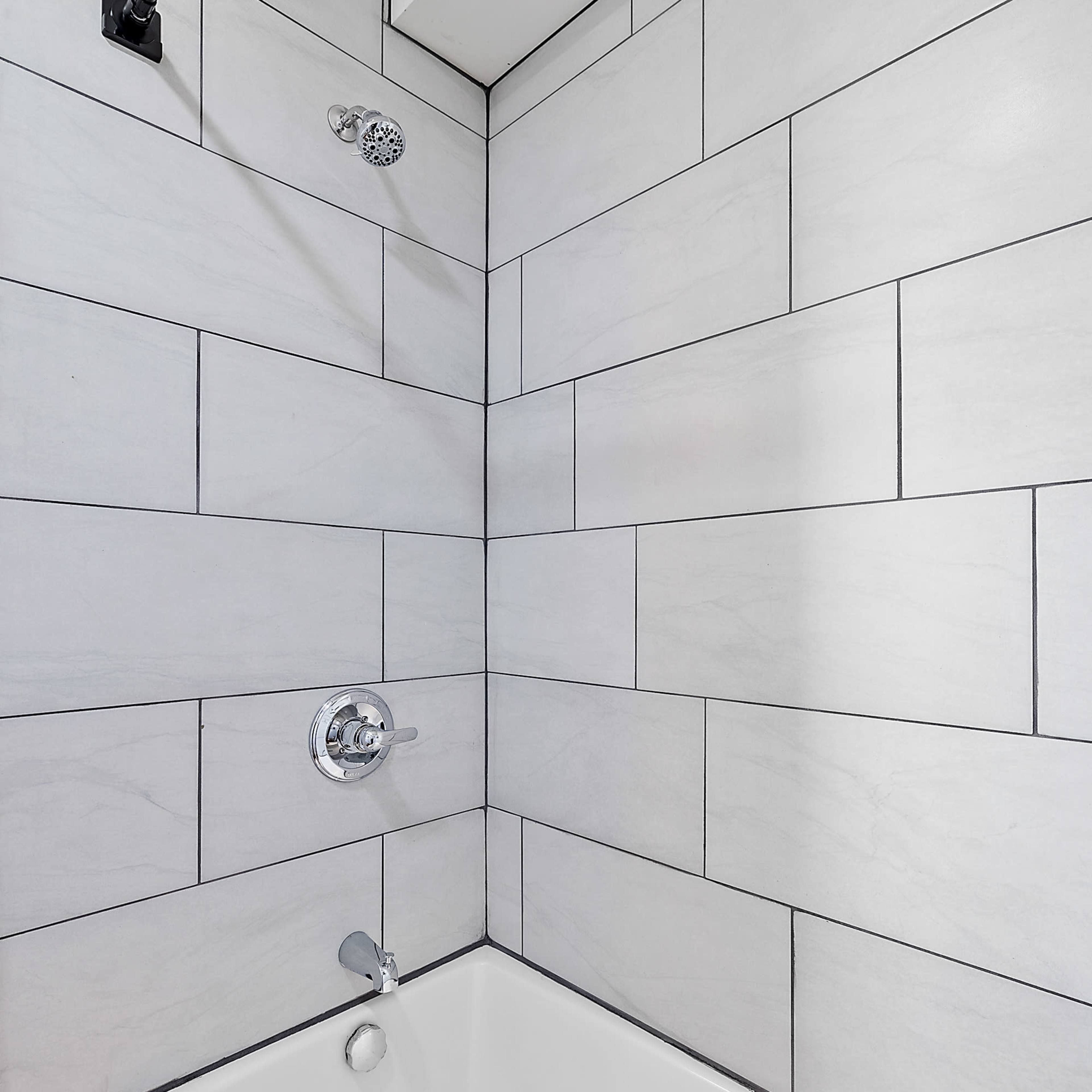 A clean bathtub with a tiled wall and a shower fixture above it.