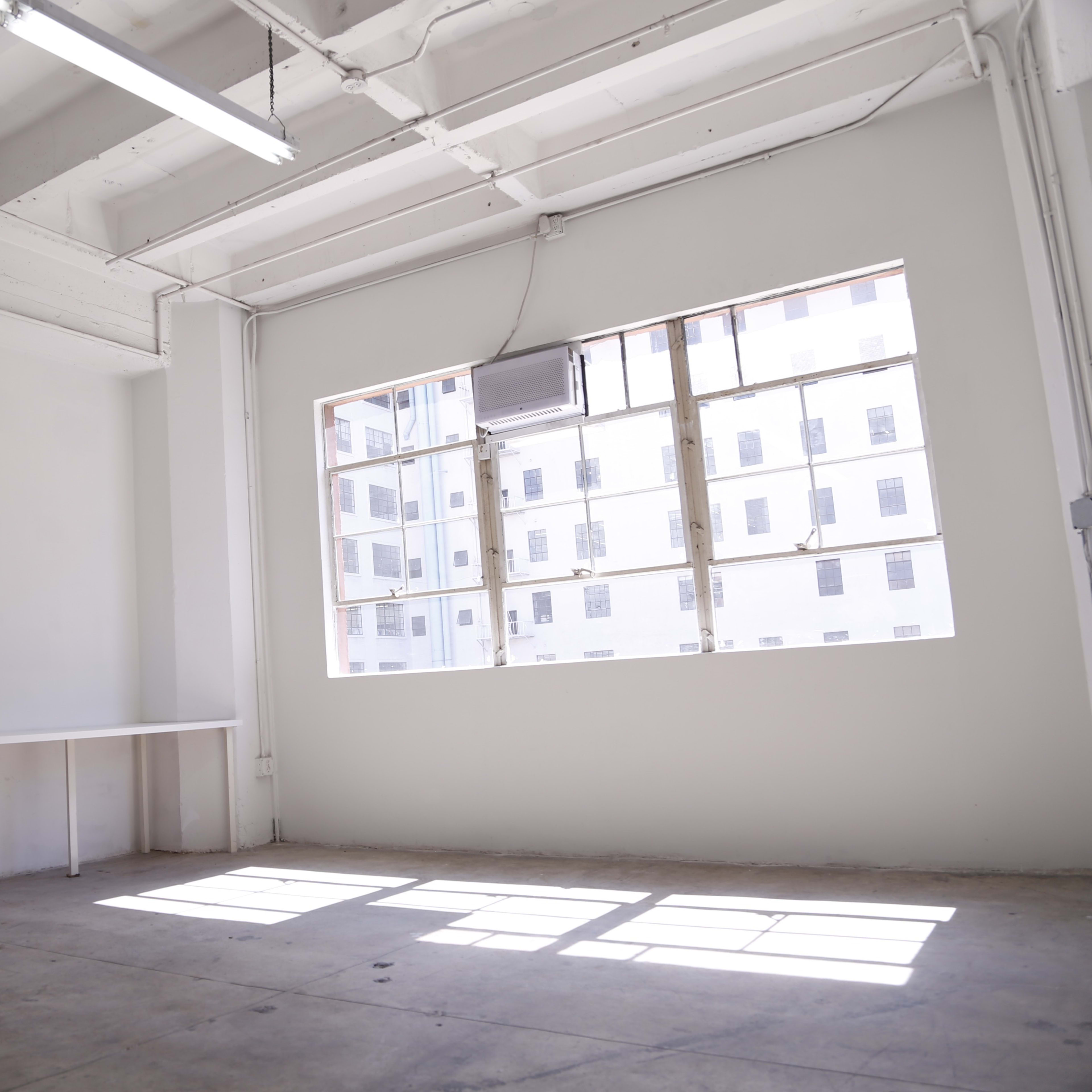 A spacious, empty room with white walls and a large window providing natural light.