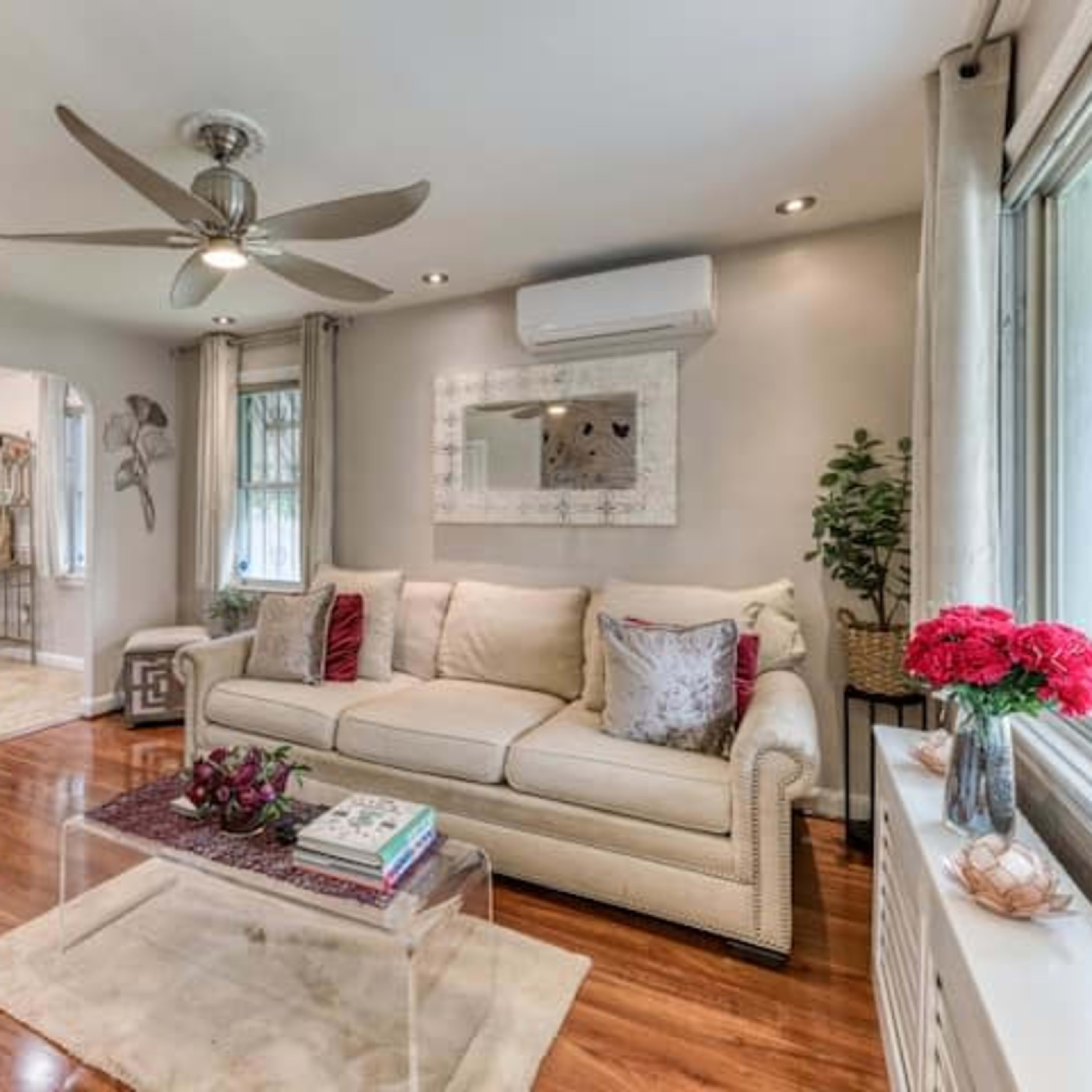 A living room with a light-colored sofa, a flat-screen television mounted on the wall, and a coffee table on a rug.