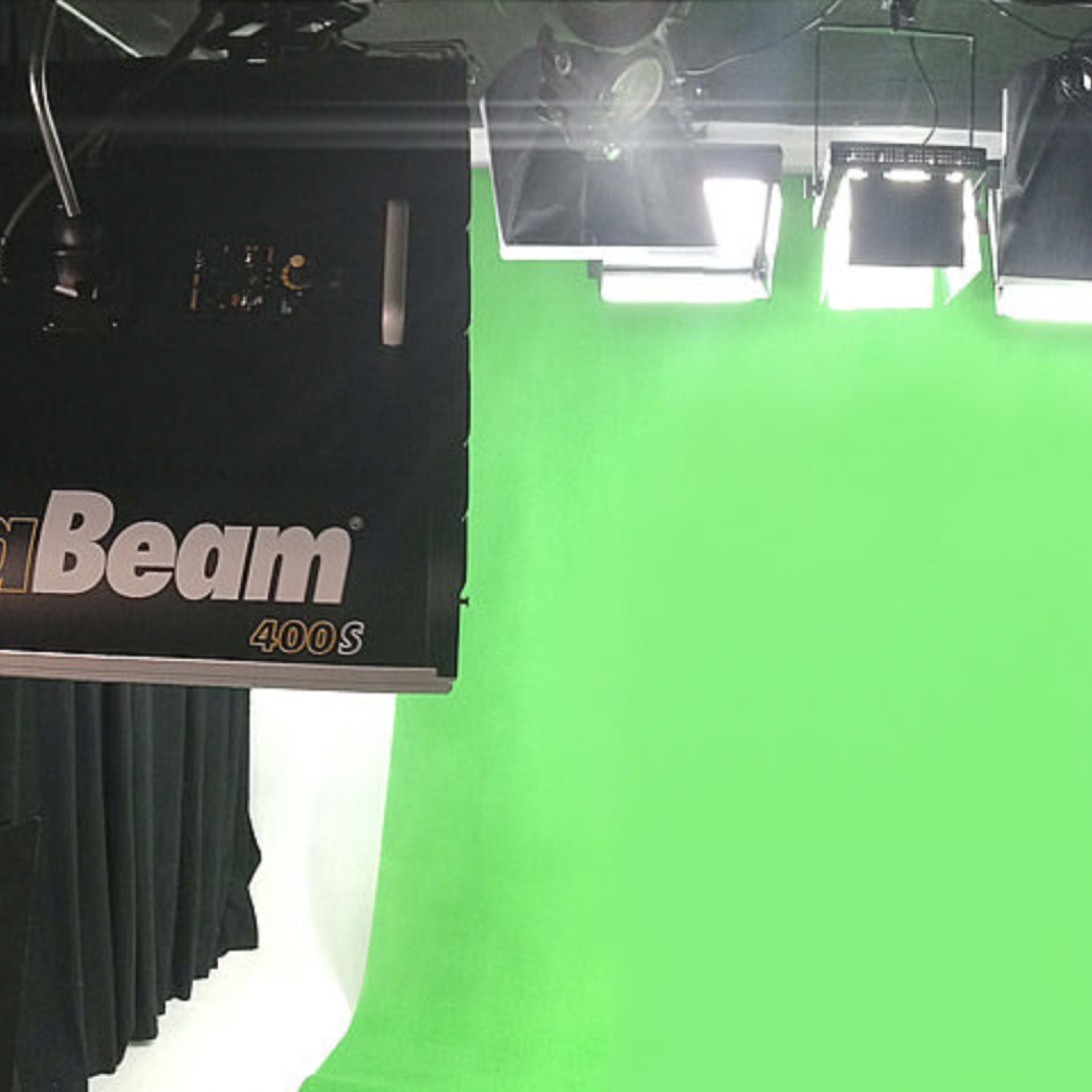 A photography studio with green screen backdrops and professional lighting equipment suspended from the ceiling.