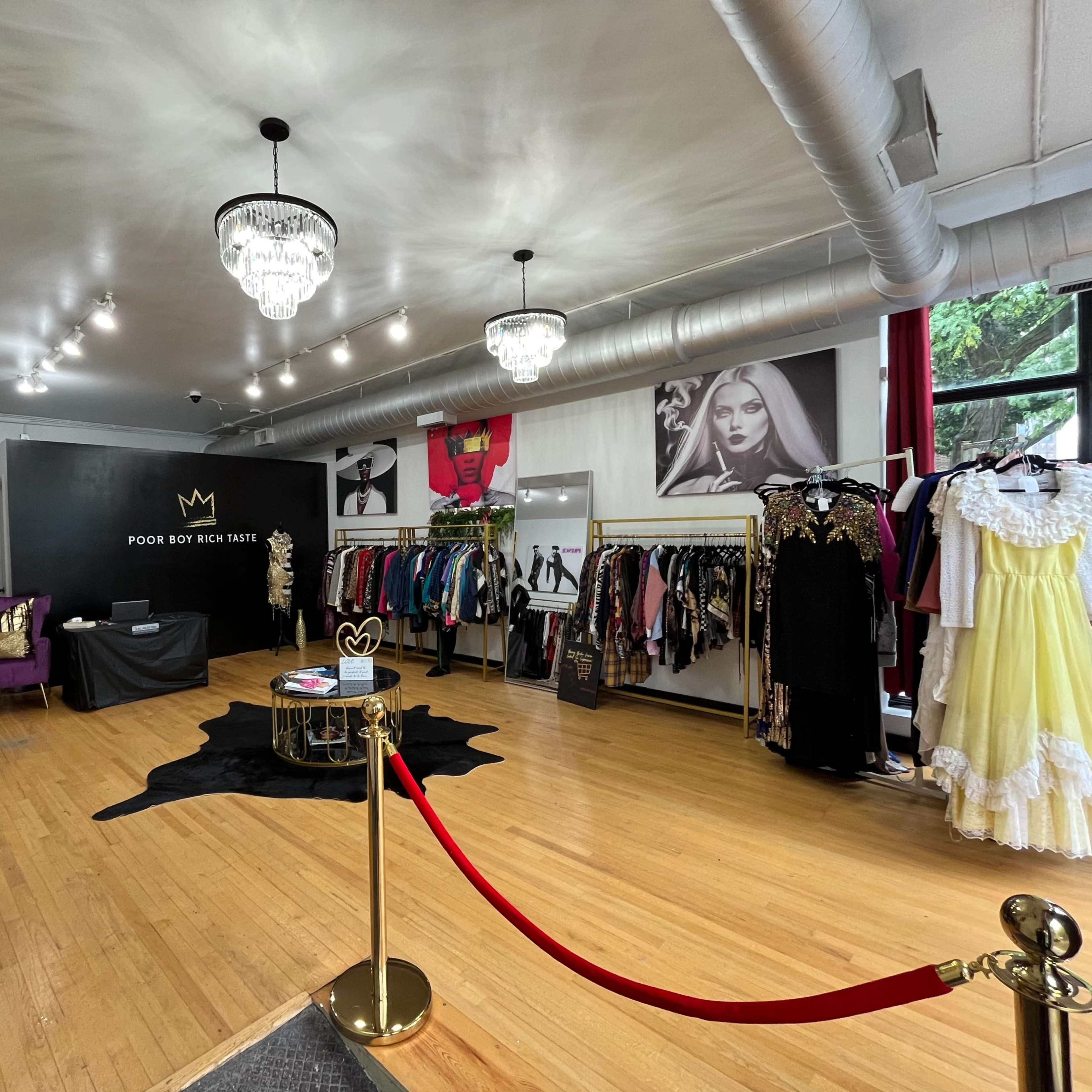 An interior of a fashion boutique featuring clothing racks, a black display wall with a logo, and a red rope barrier at the entrance.