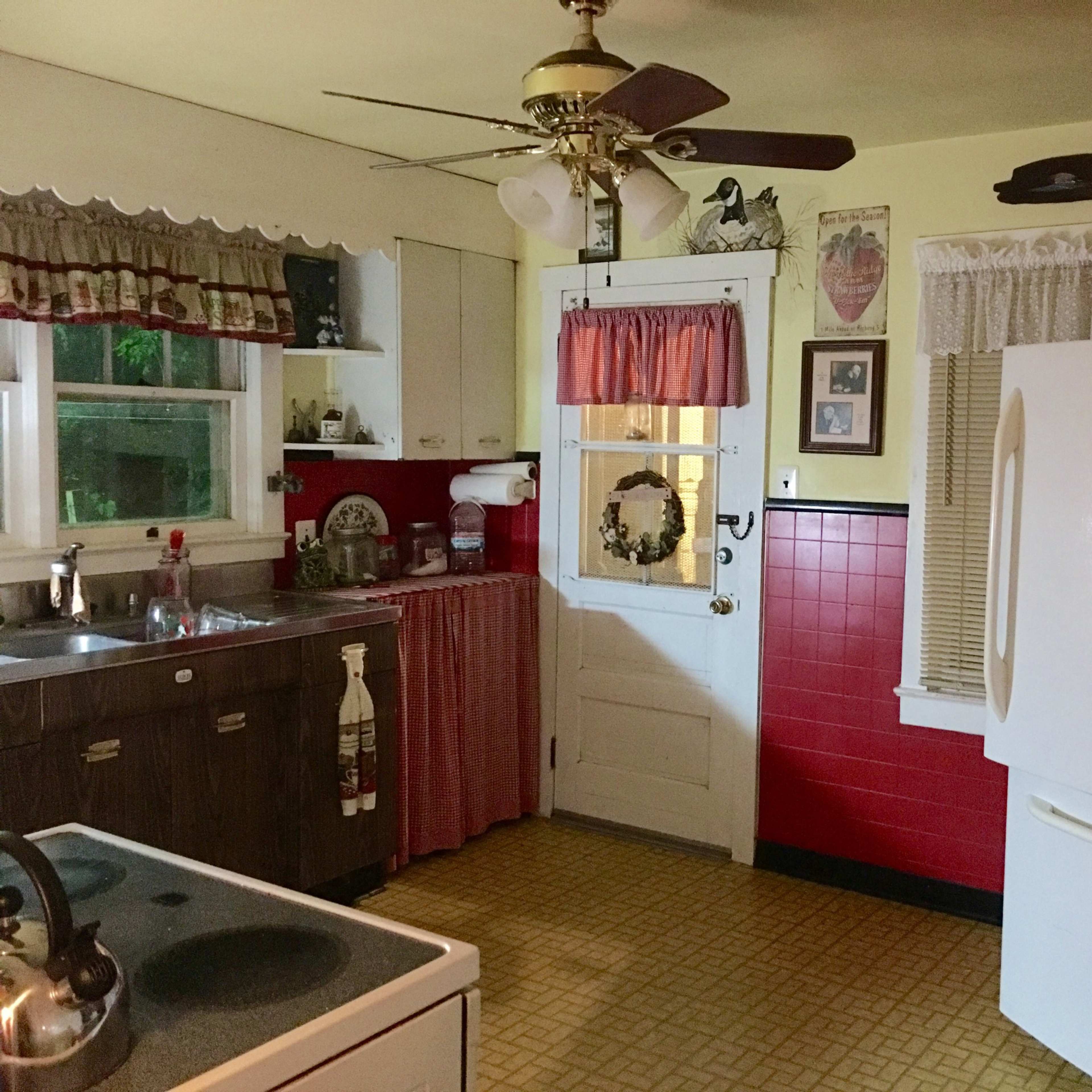 A kitchen with wooden cabinets, a white refrigerator, a red wall, and a door leading outside.