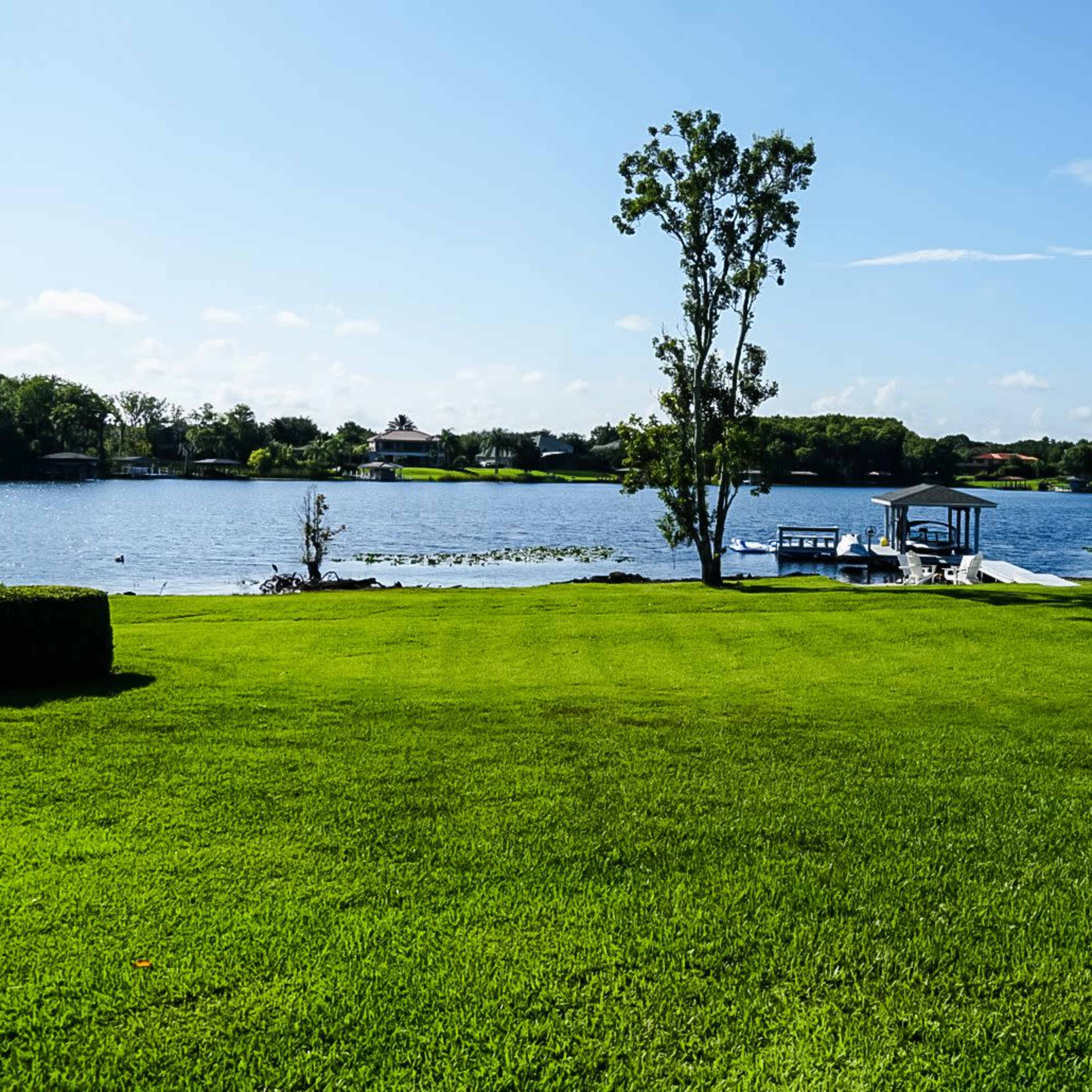 A well-maintained lawn leads to a calm lake surrounded by trees and a small dock with boats.