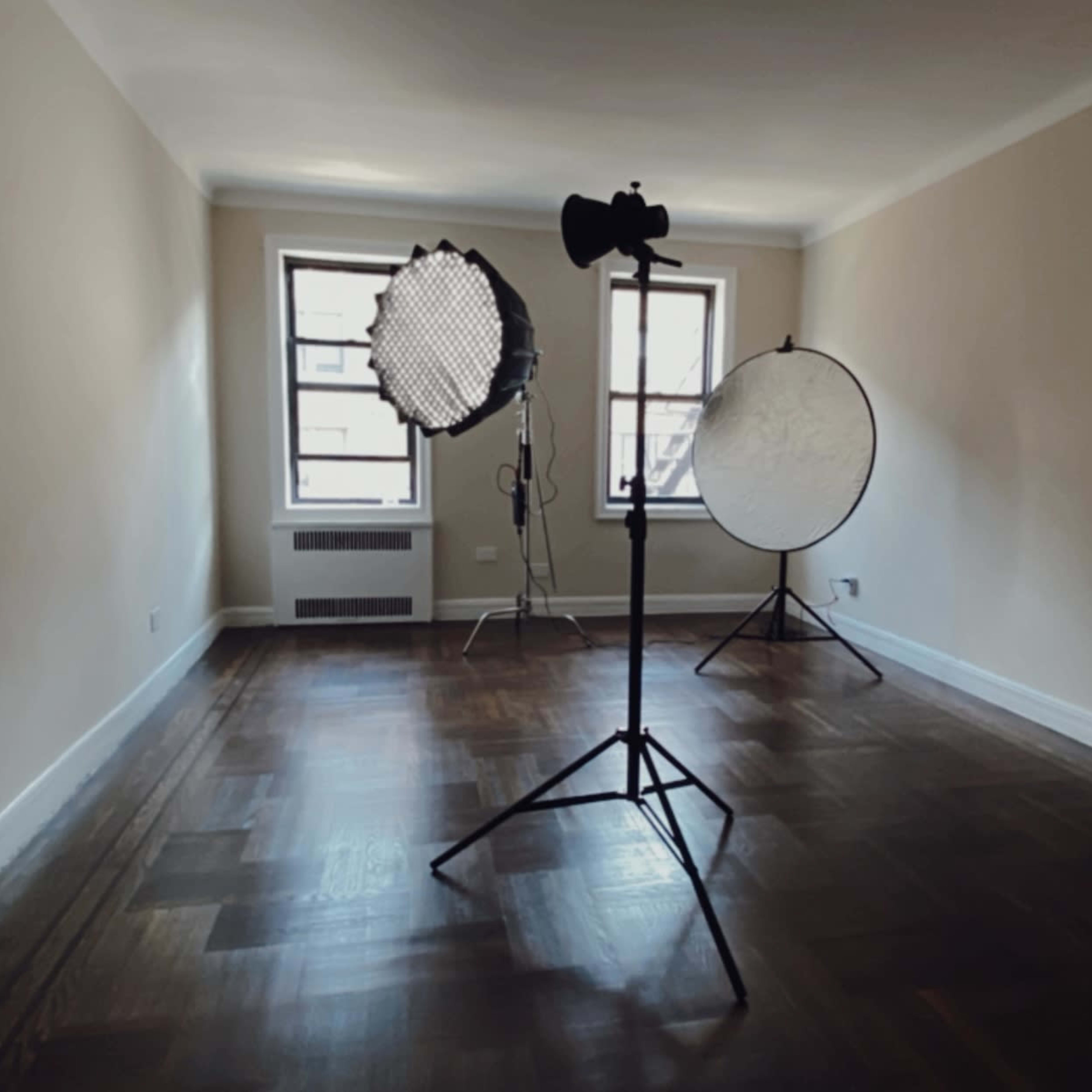 An empty room with hardwood floors is set up for a photo shoot, featuring light stands and softboxes.