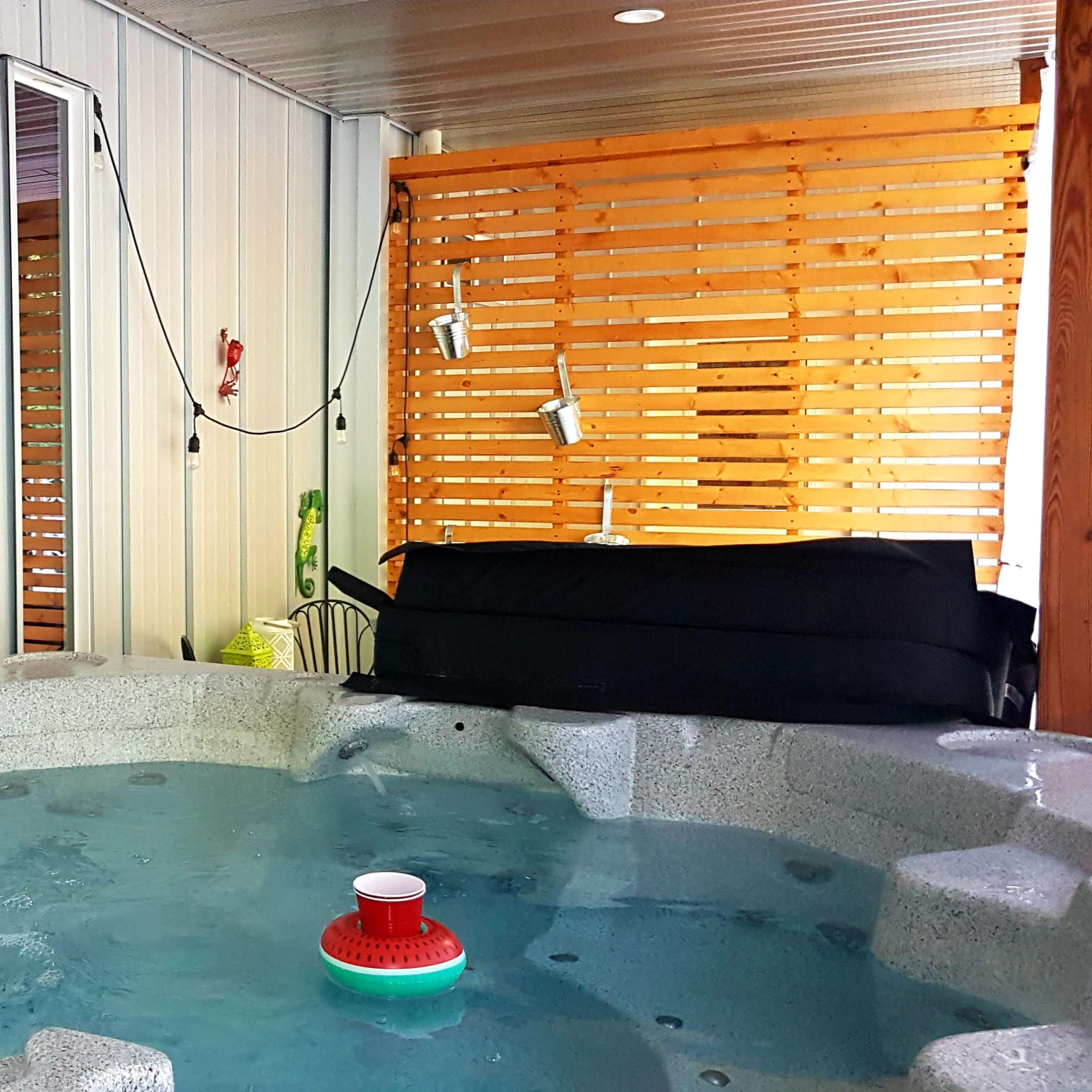 A hot tub situated in a partially enclosed area with wooden paneling and hanging lights.