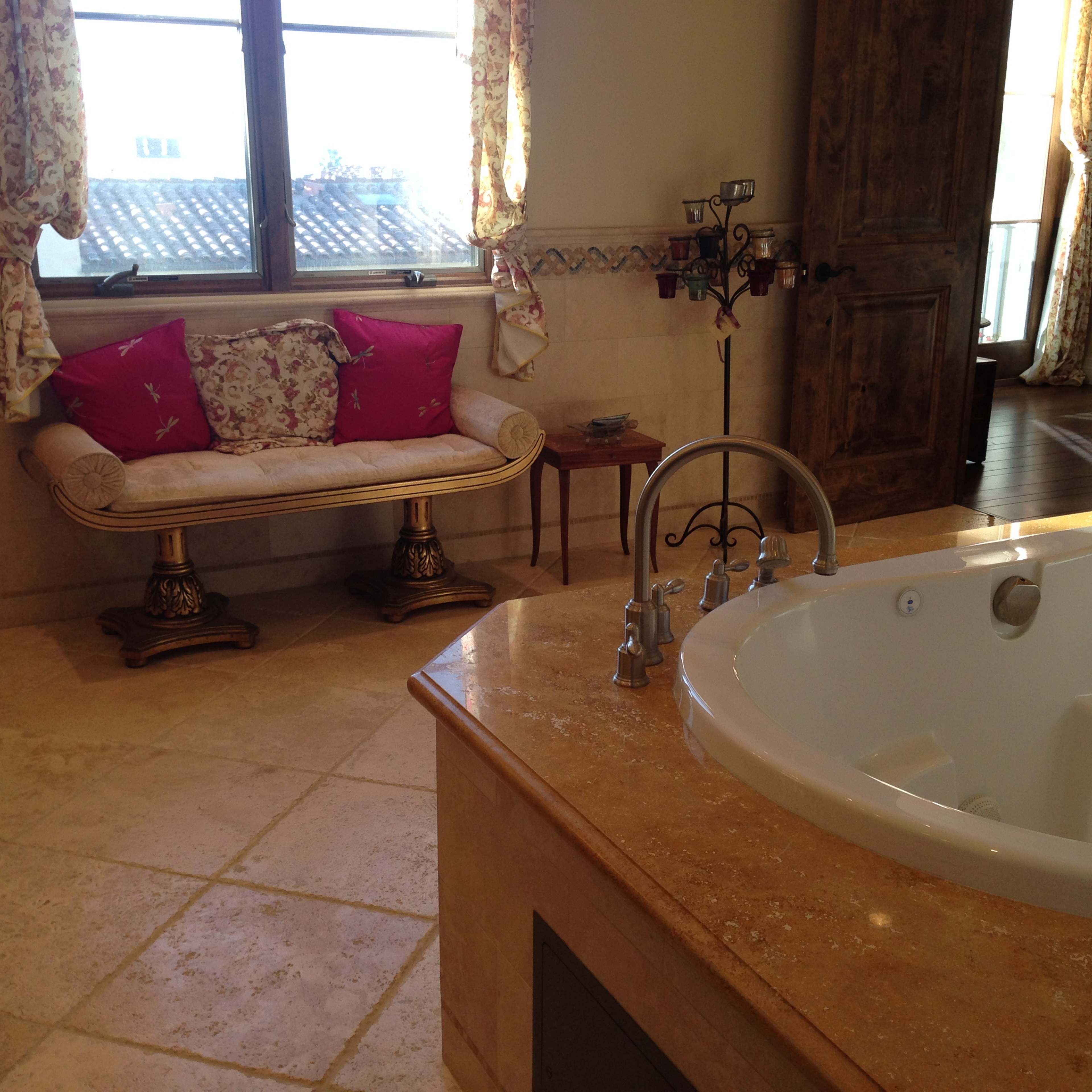 A spacious bathroom featuring a large bathtub, a small couch with decorative pillows, and a window allowing natural light.