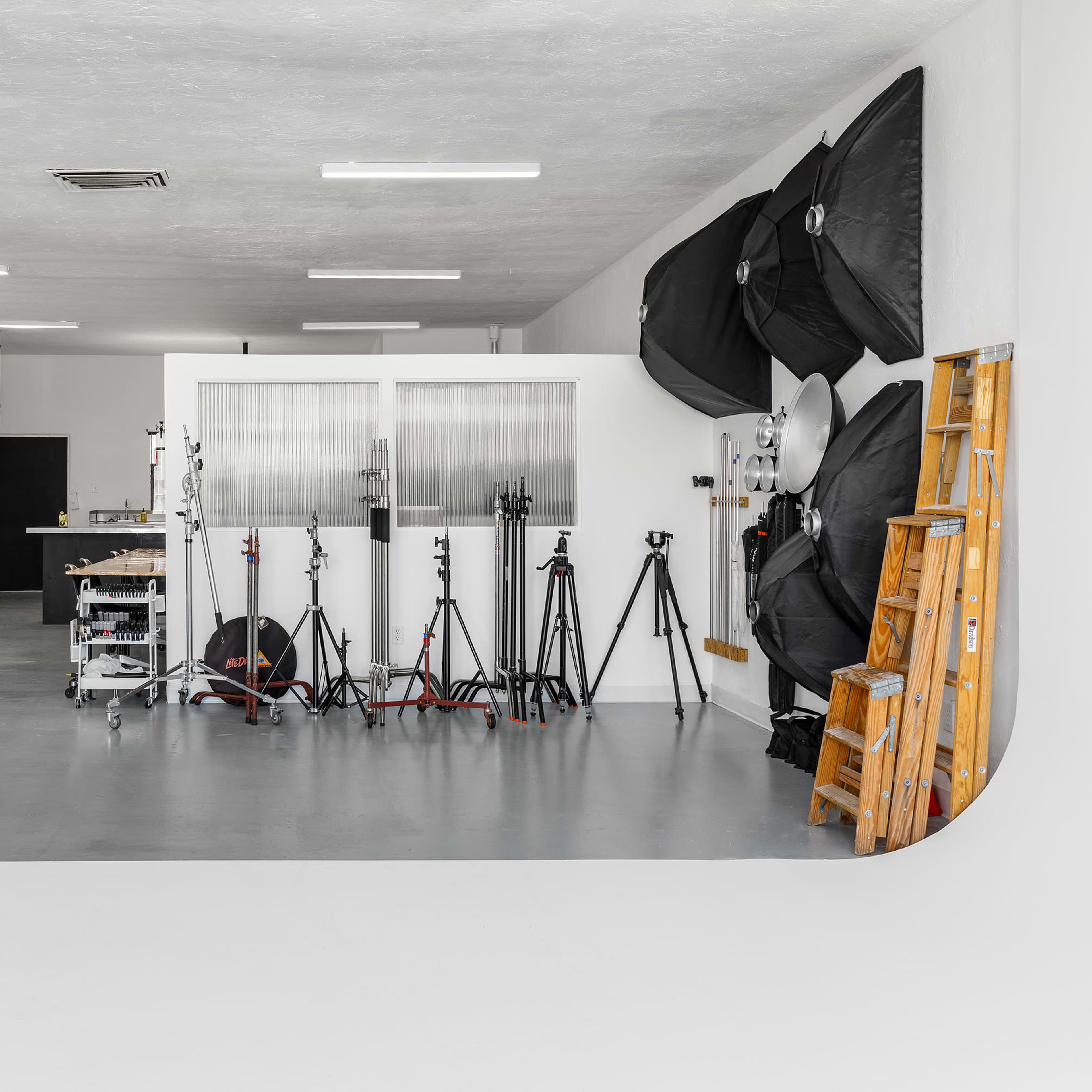 A spacious photography studio featuring various lighting equipment, tripods, and a clean backdrop area.