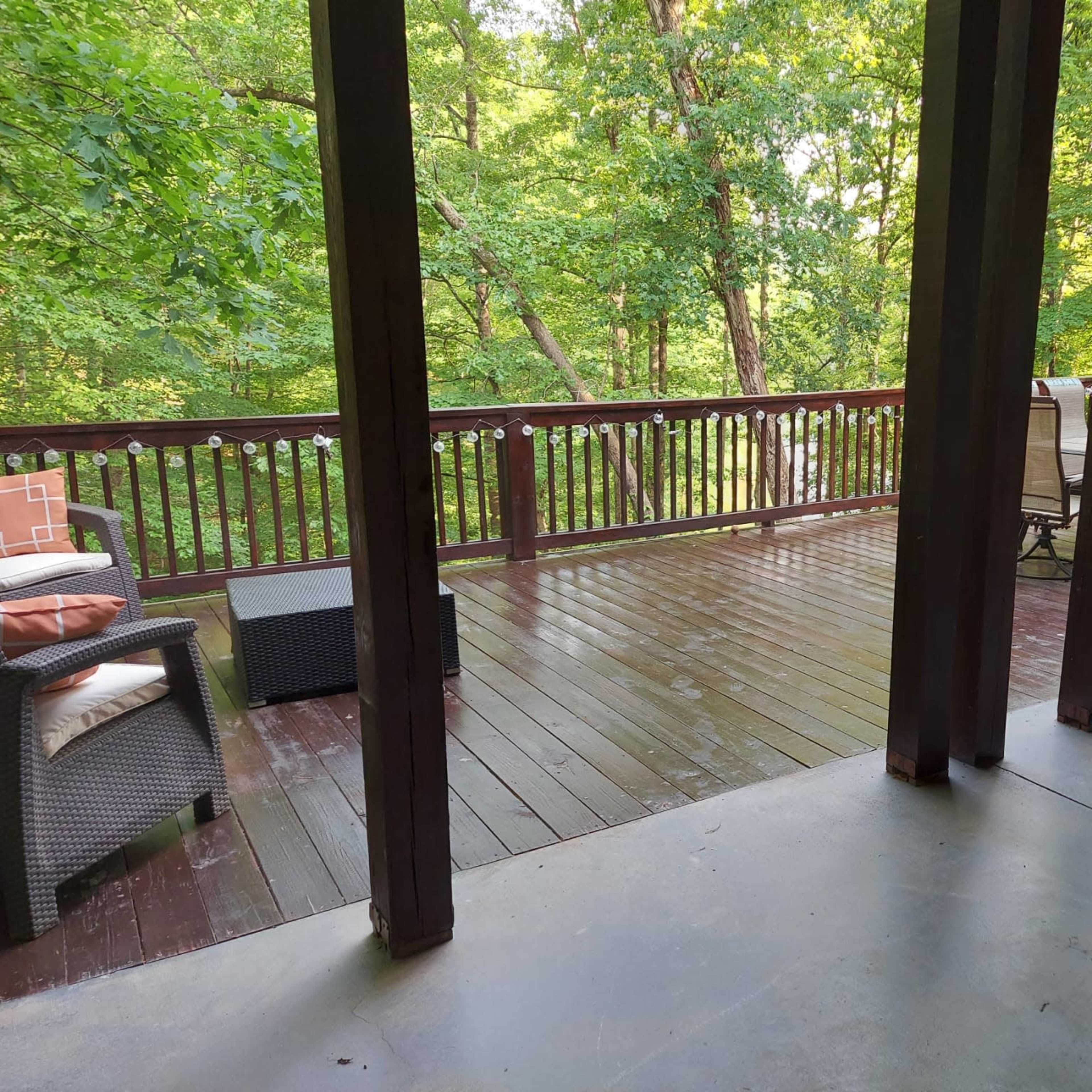 A spacious wooden deck surrounded by greenery, featuring outdoor furniture and a clear view of the forest.