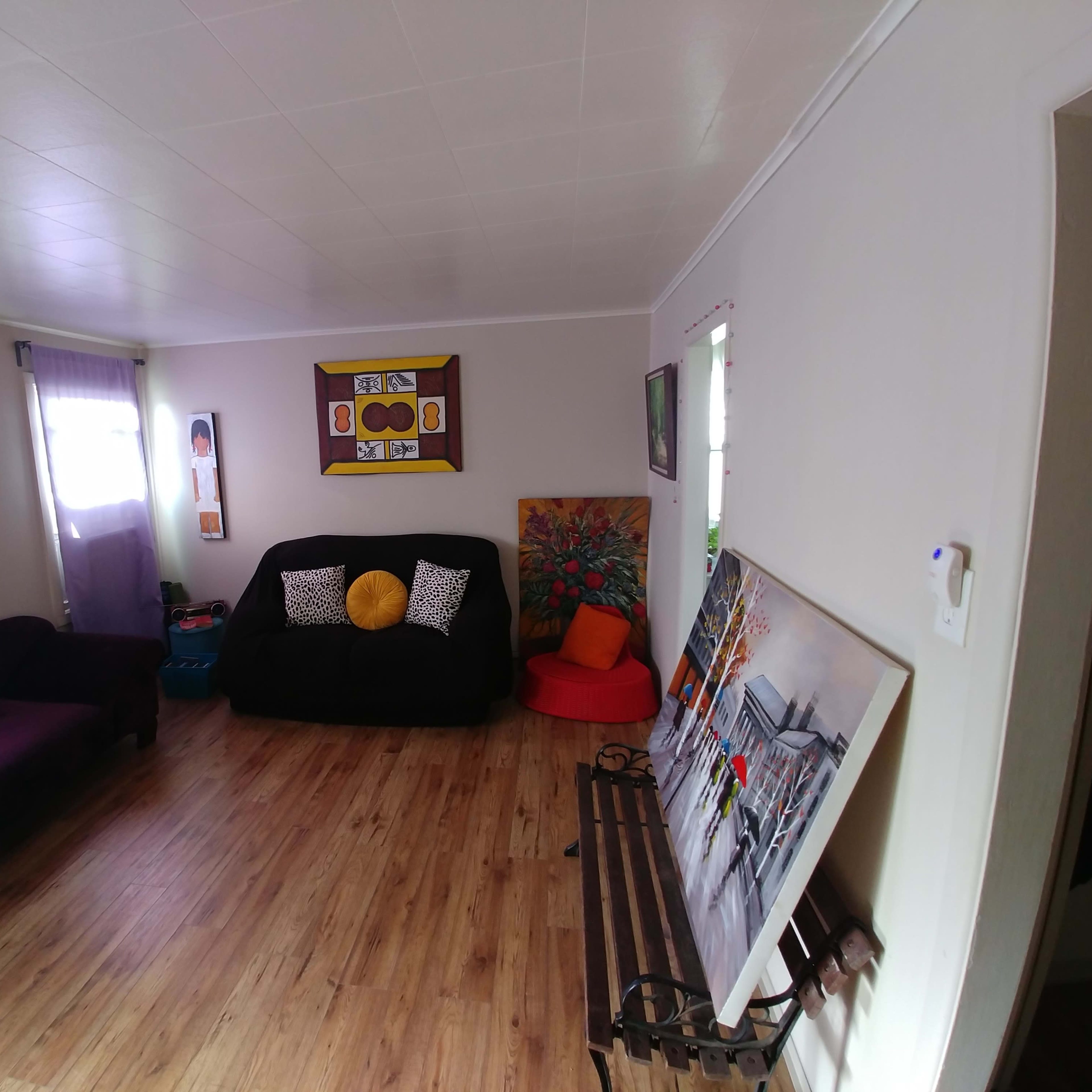 A living room featuring a purple couch, black seating area, colorful artwork on the walls, and a wooden bench near the entrance.