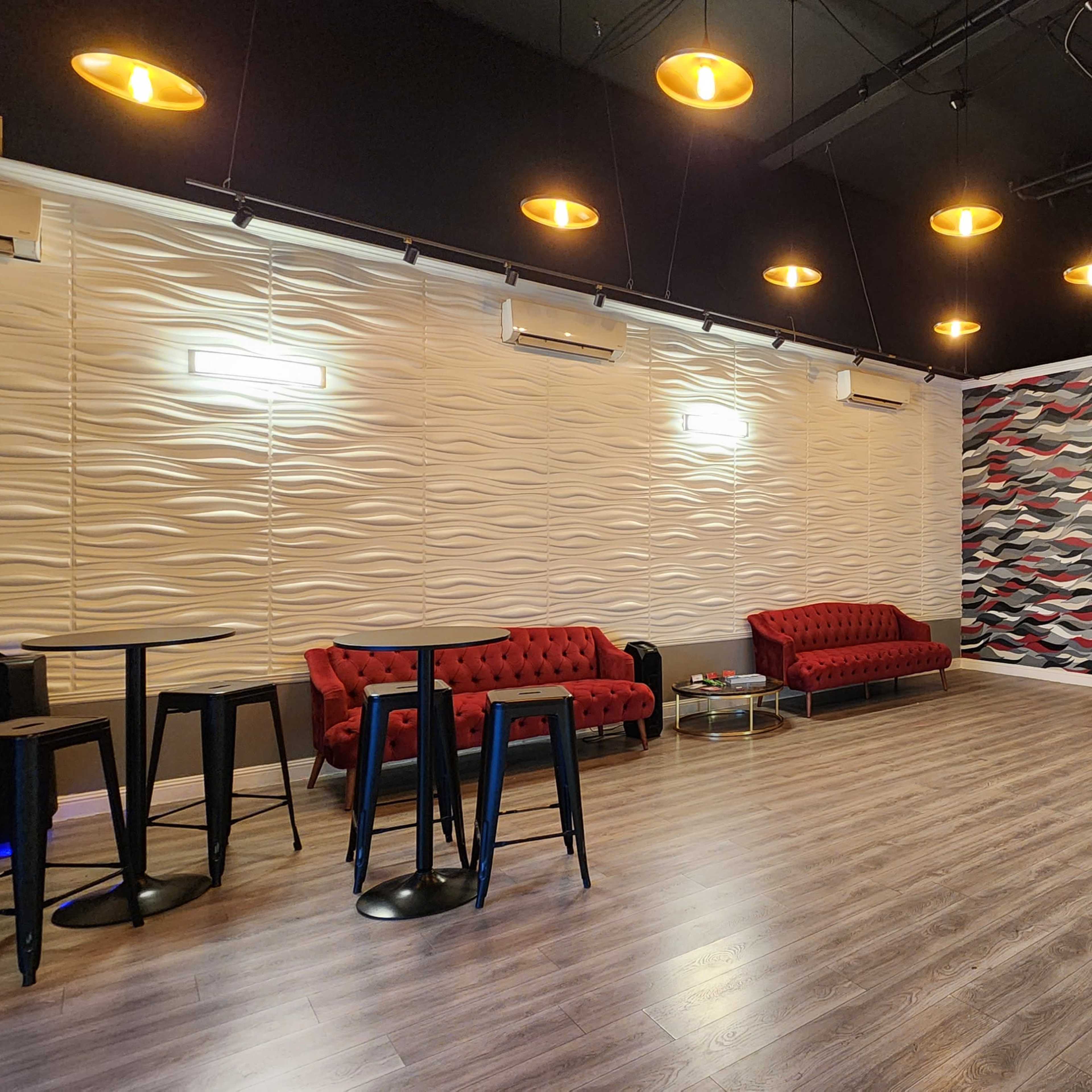 A modern event space with two red sofas, a stage area, and wall-mounted speakers, illuminated by hanging lights.
