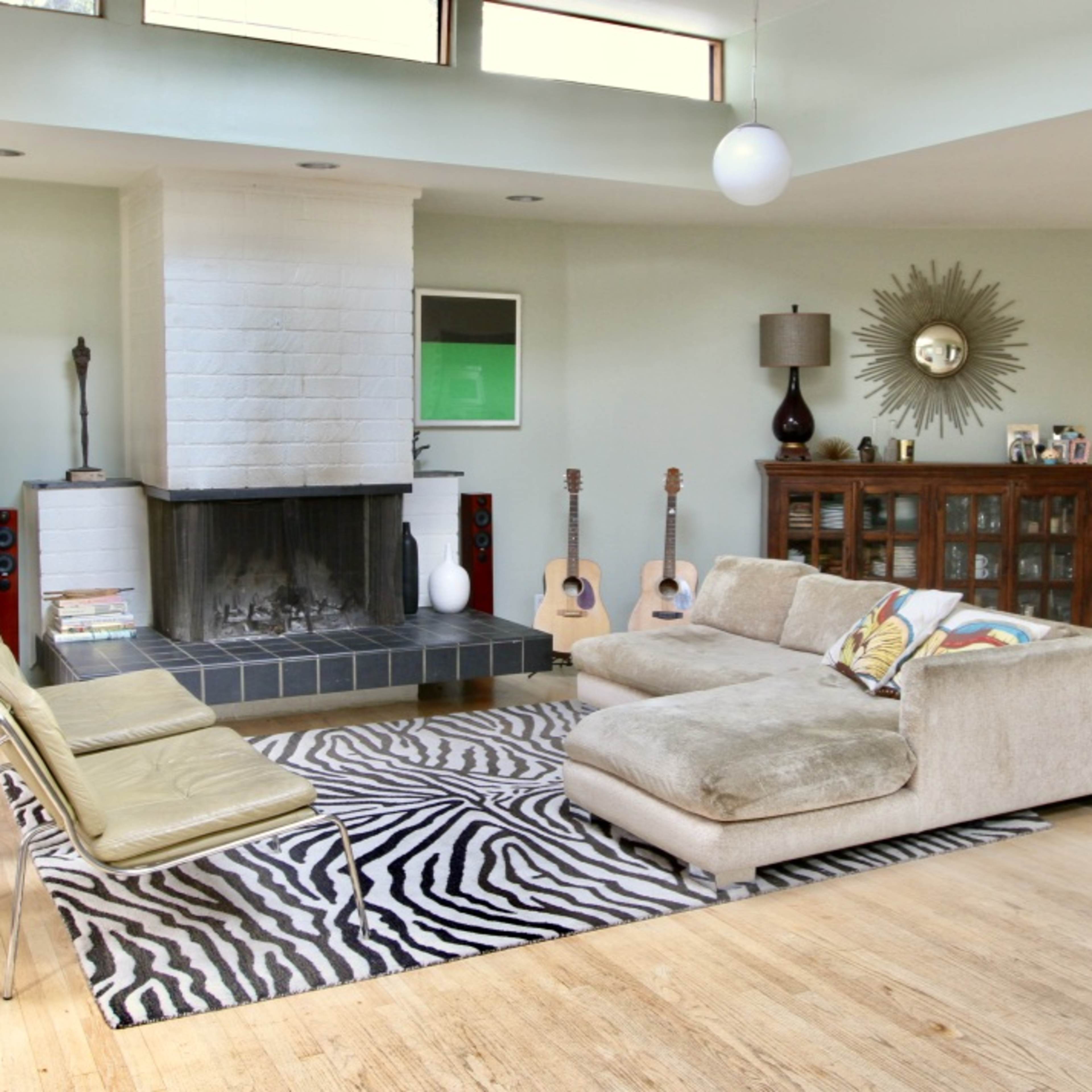 A spacious living room featuring a fireplace, a sectional sofa, a zebra-striped rug, and a combination of musical instruments and decorative furniture.