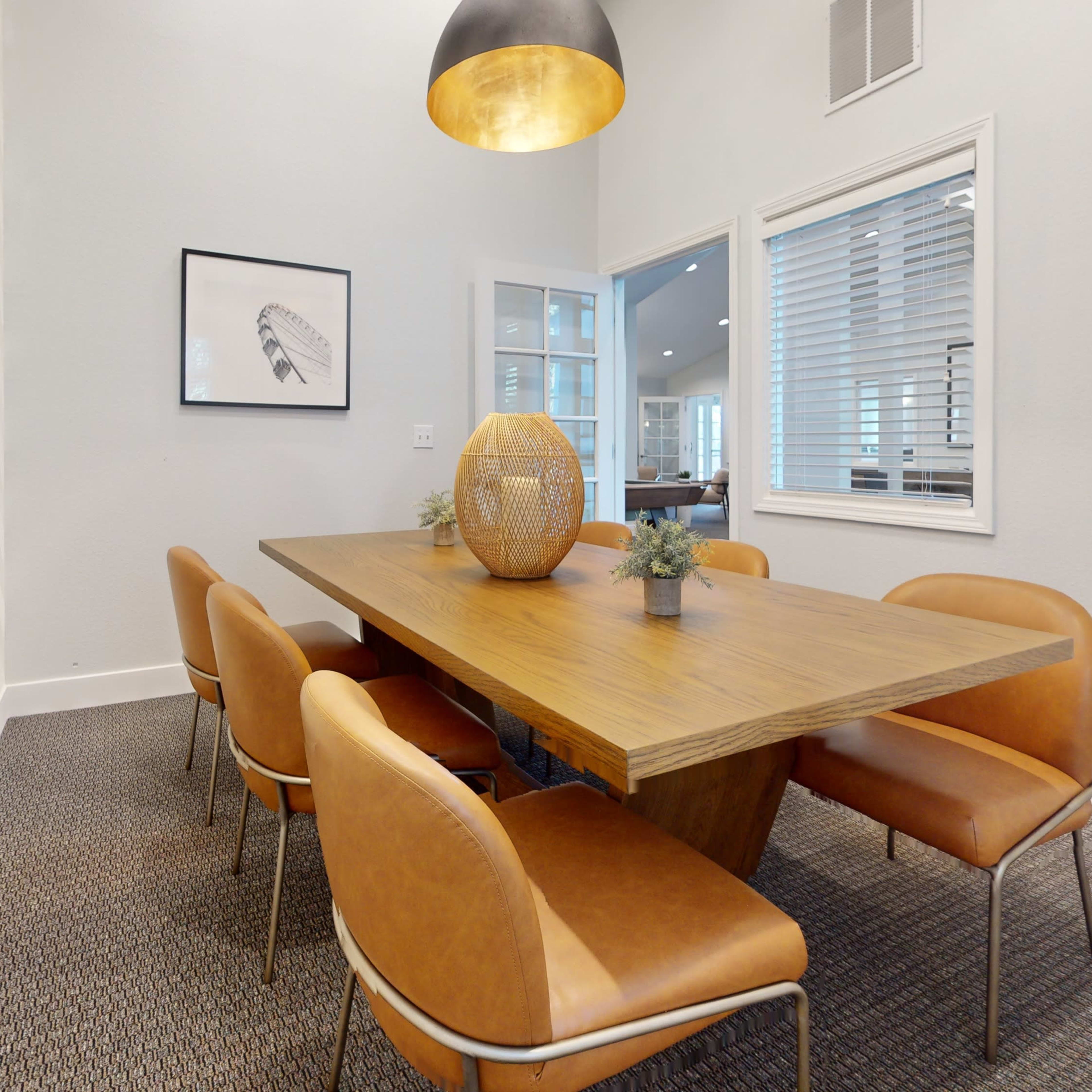 A modern dining area features a wooden table surrounded by brown leather chairs, with a pendant light hanging above and wall art on display.