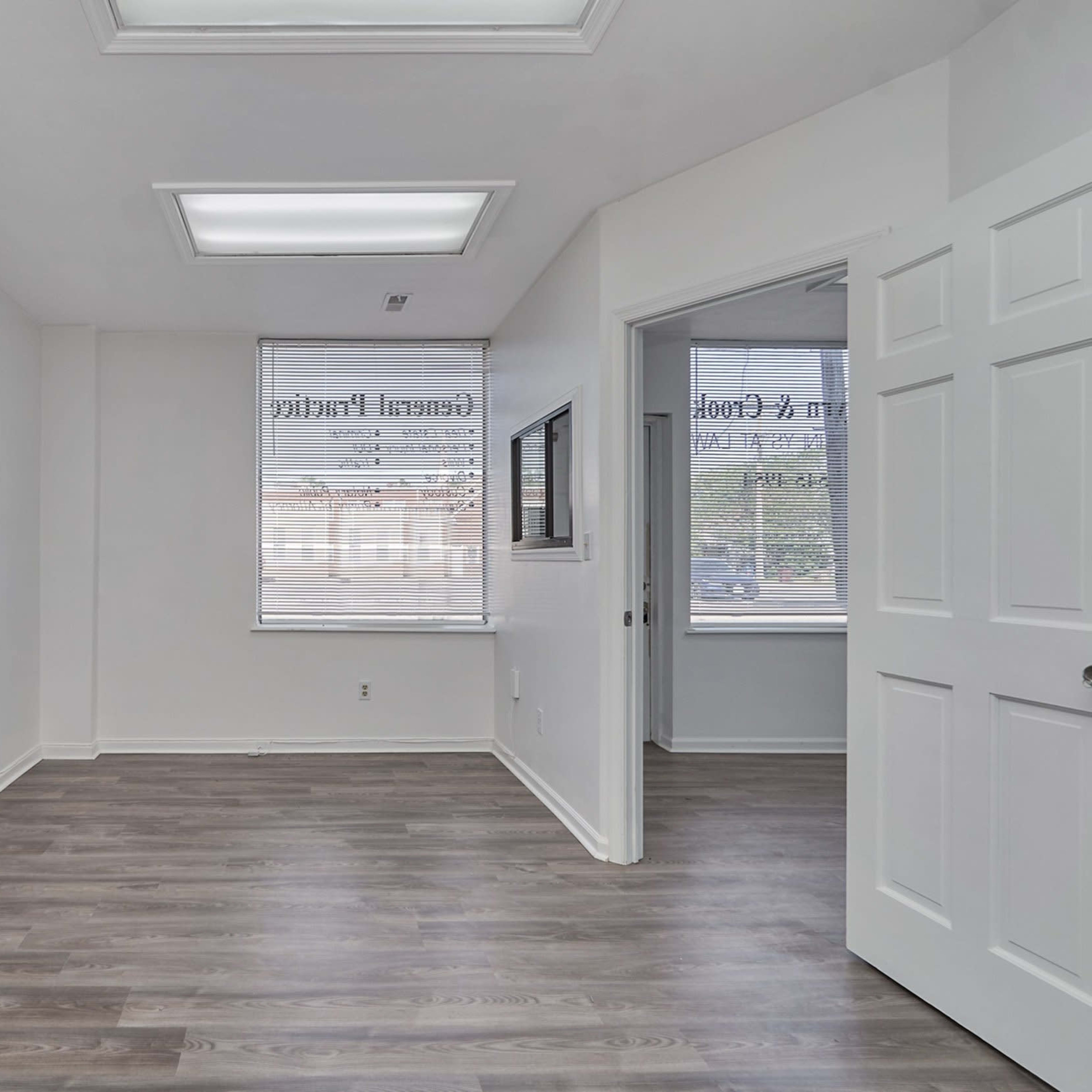 A vacant office space with white walls, hardwood-like flooring, and a door leading to another room.