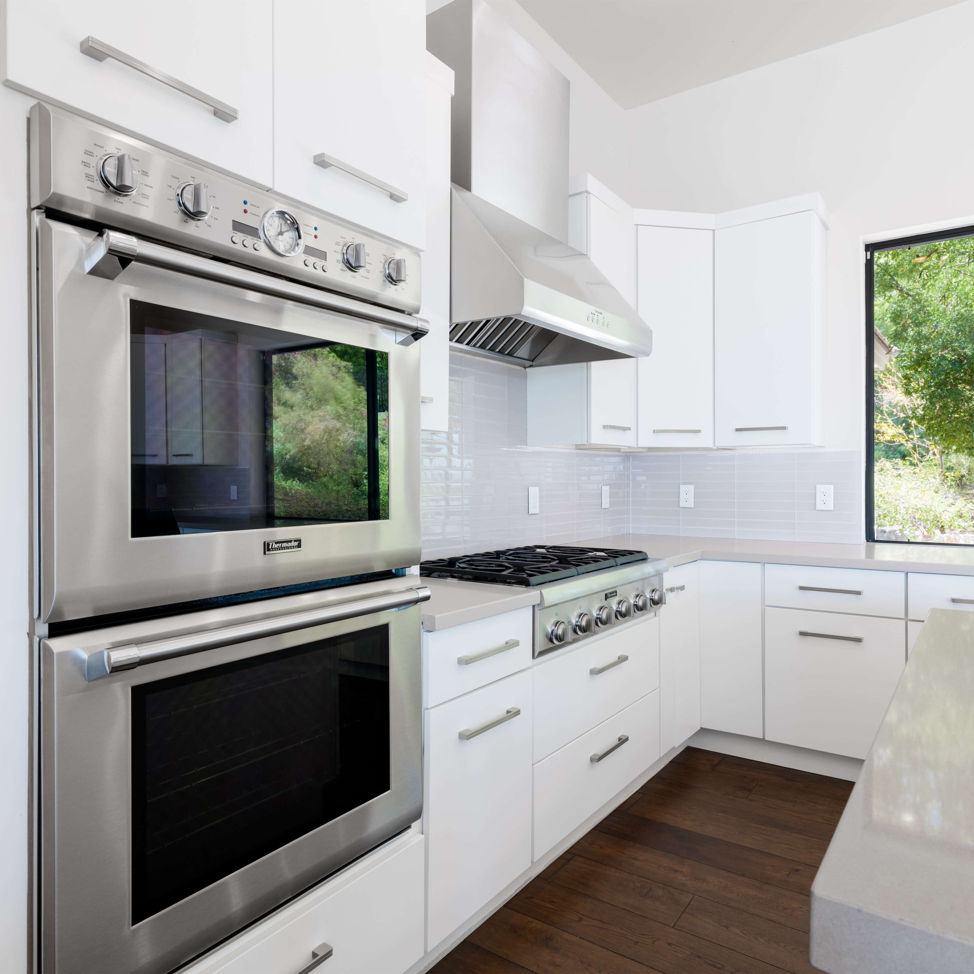 A modern kitchen with stainless steel appliances, including an oven and a gas range, set against white cabinetry and a light backsplash.