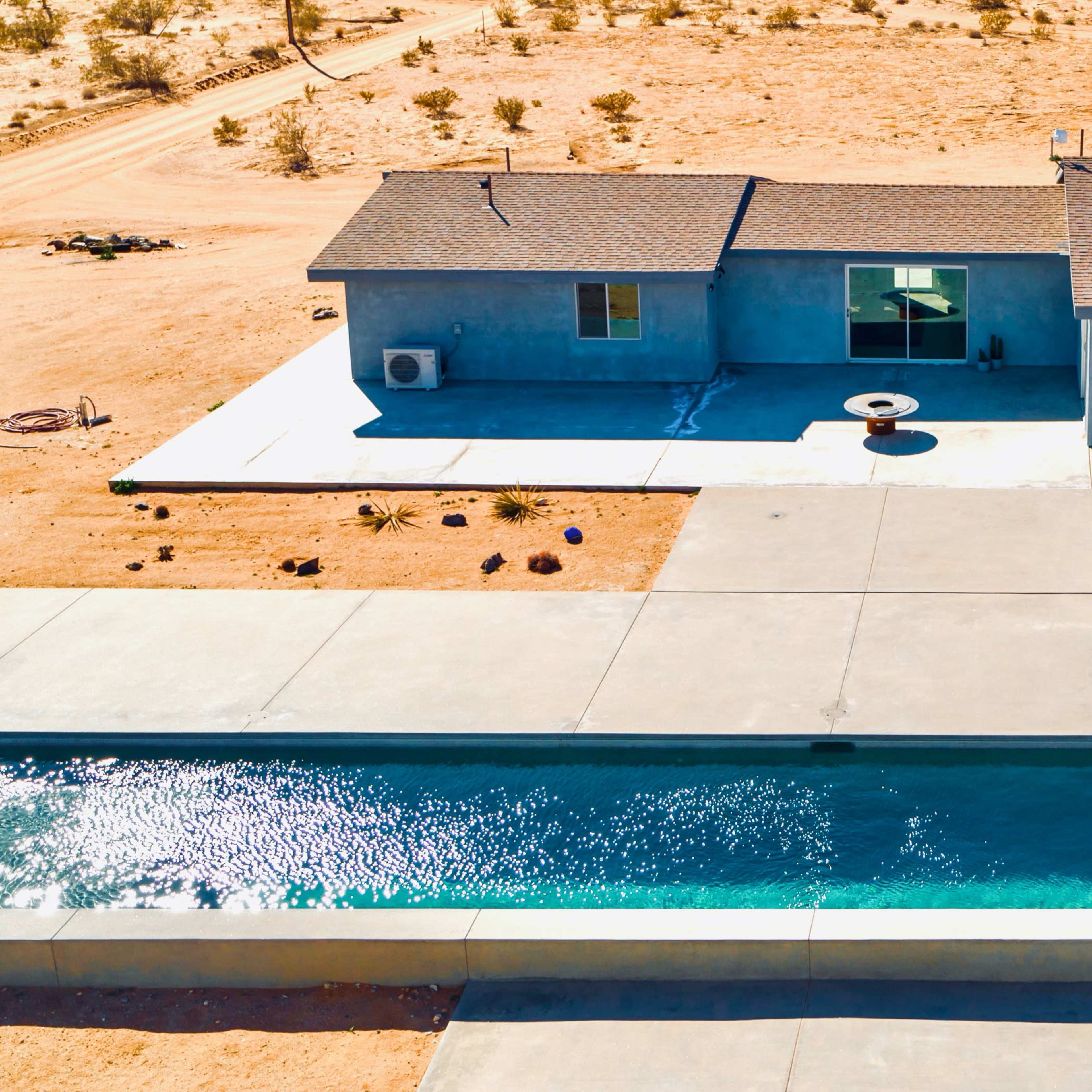 A modern single-story house with large windows next to a swimming pool in a desert landscape.