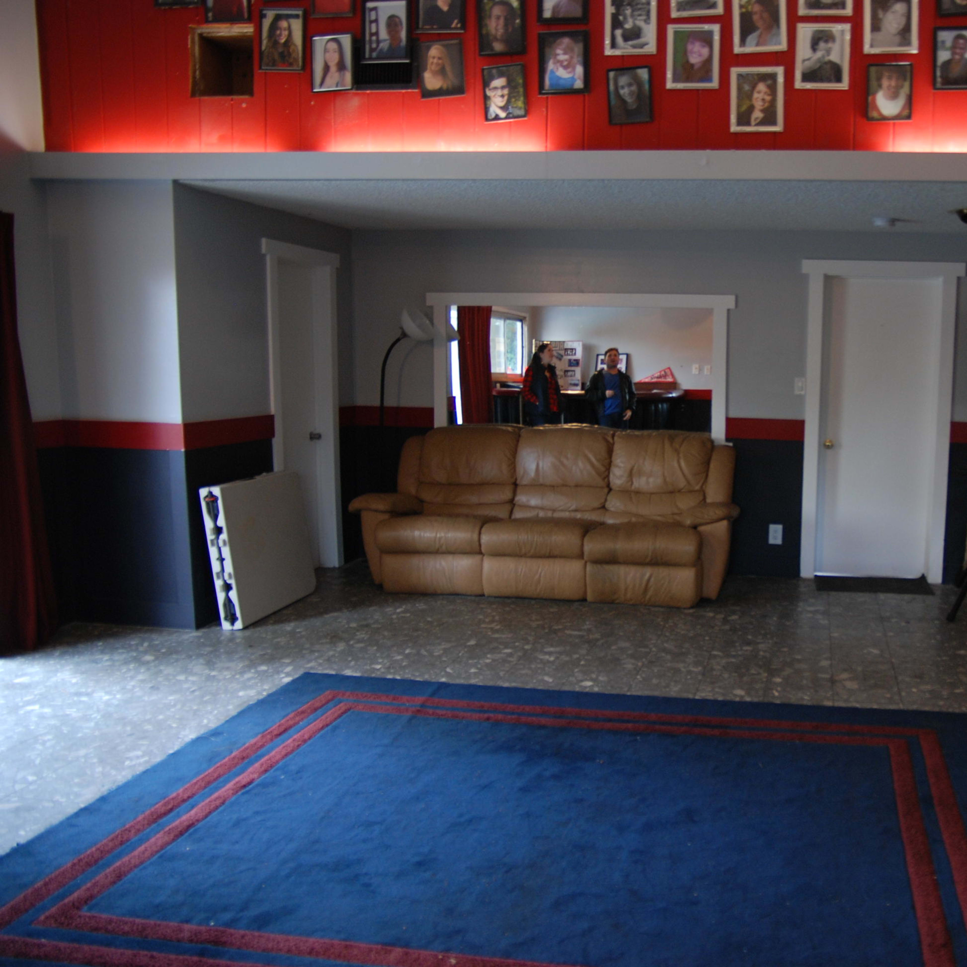 A spacious room with a blue rug, brown leather couch, a green couch, and a wall adorned with a grid of framed photographs.