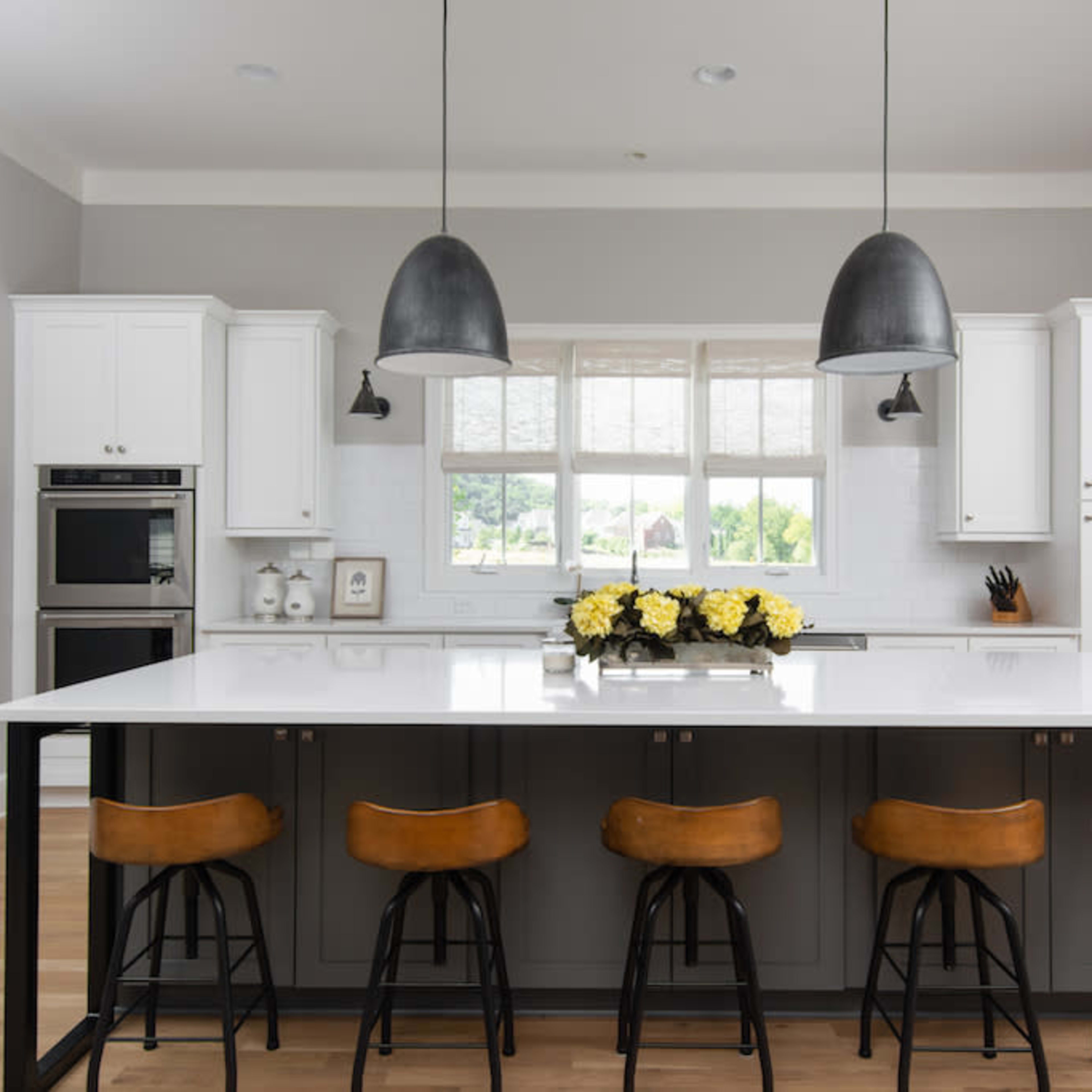 A modern kitchen features a large island with bar stools, white cabinetry, and pendant lighting above.