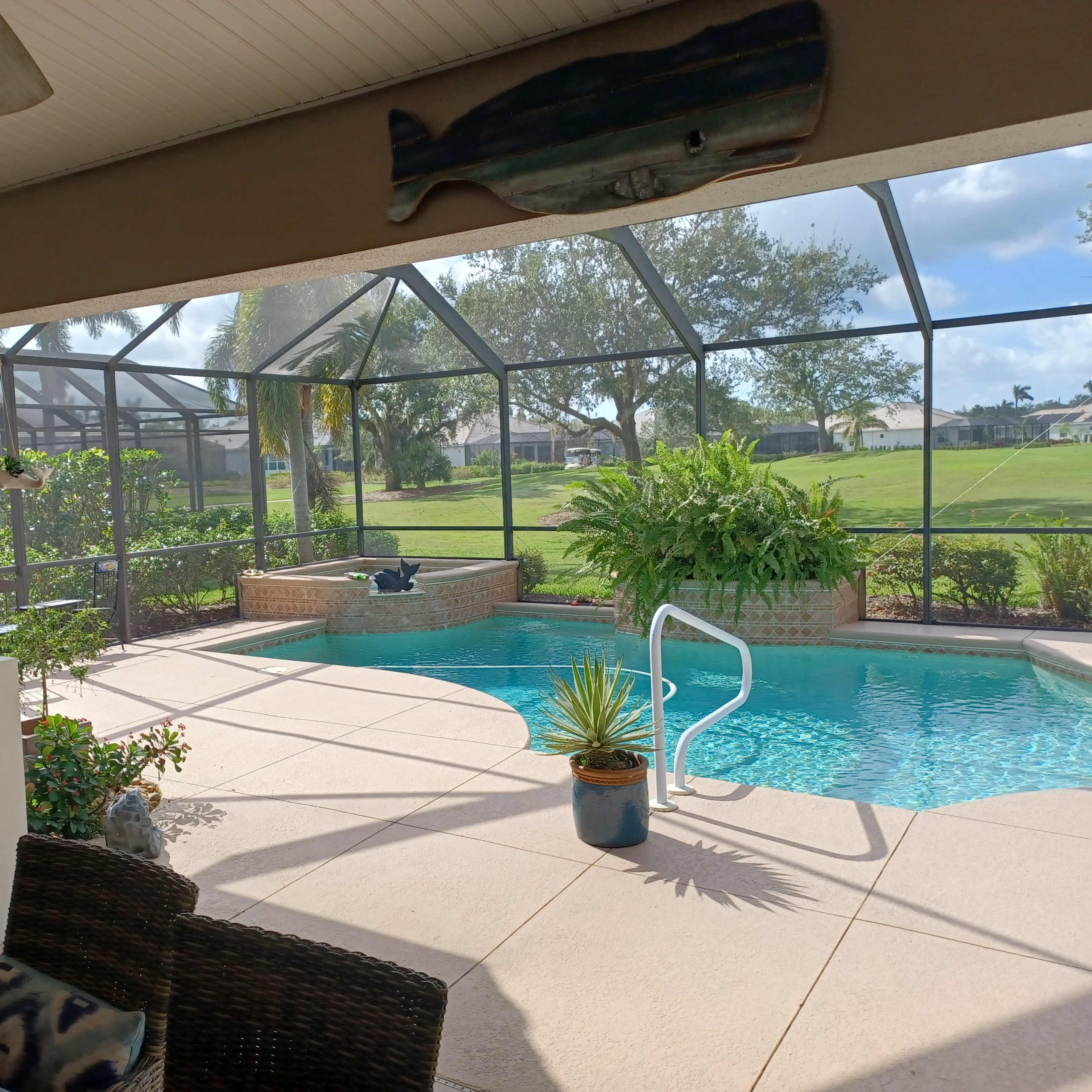 A covered patio overlooks a swimming pool surrounded by lush greenery and a screened enclosure.