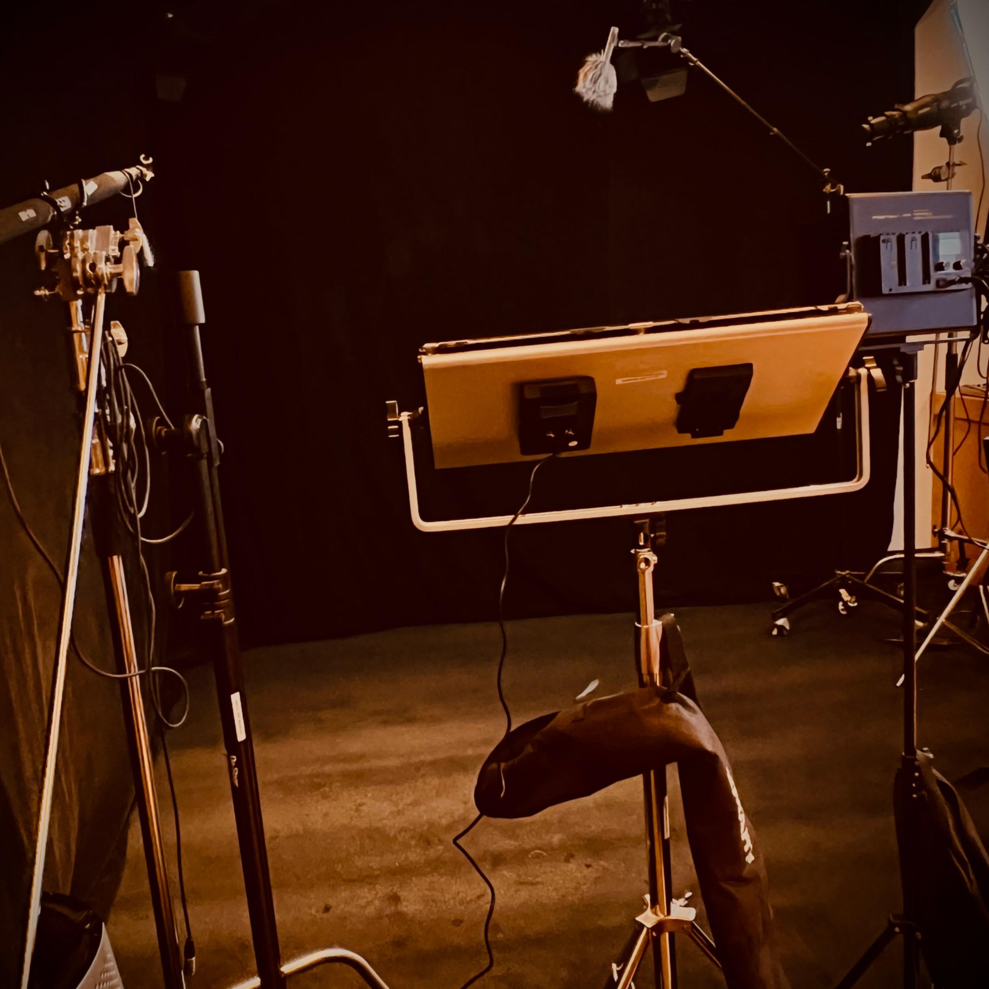 A dimly lit studio setup featuring microphones, a music stand, and various equipment positioned in front of a black backdrop.
