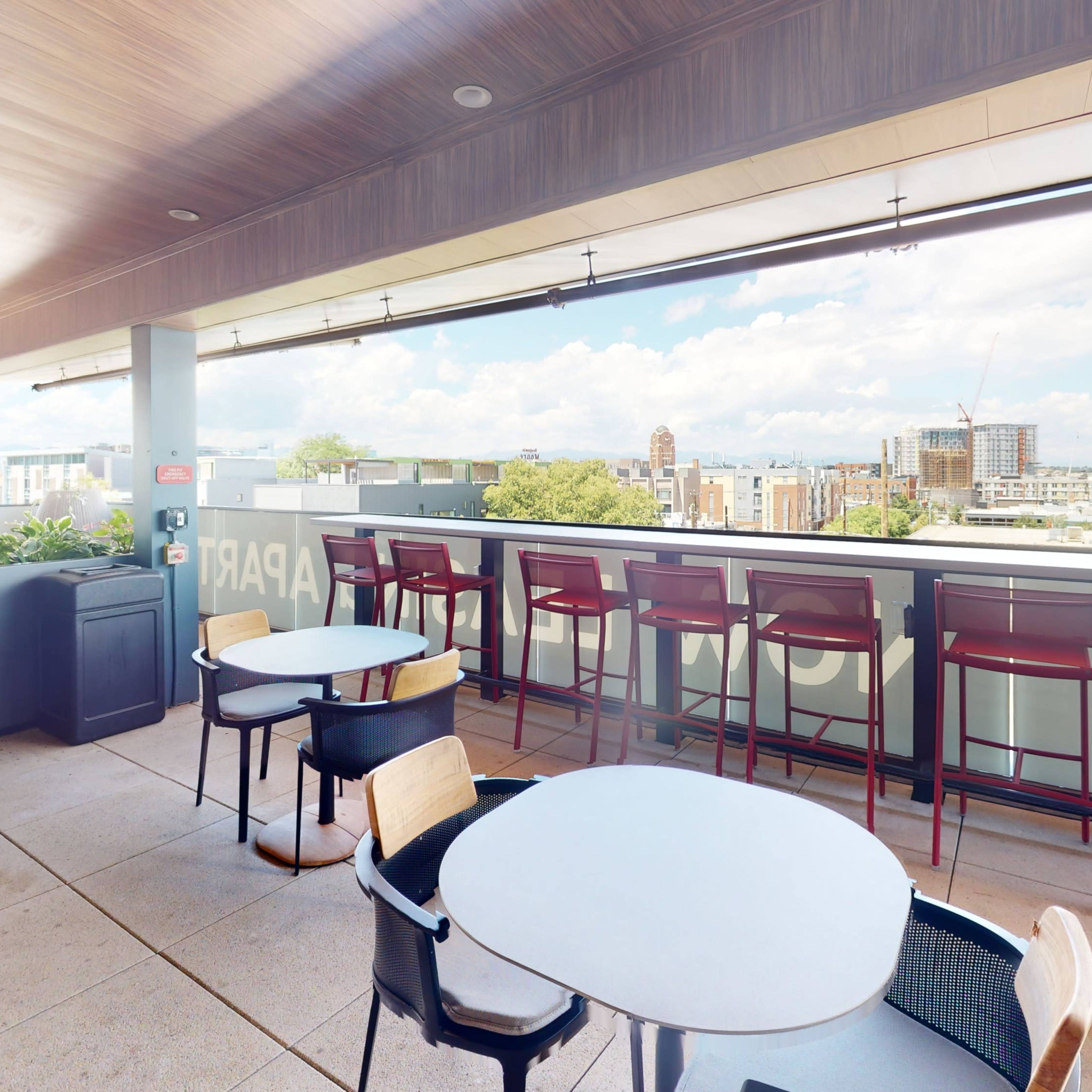 A rooftop terrace with several tables and chairs overlooking a city skyline.