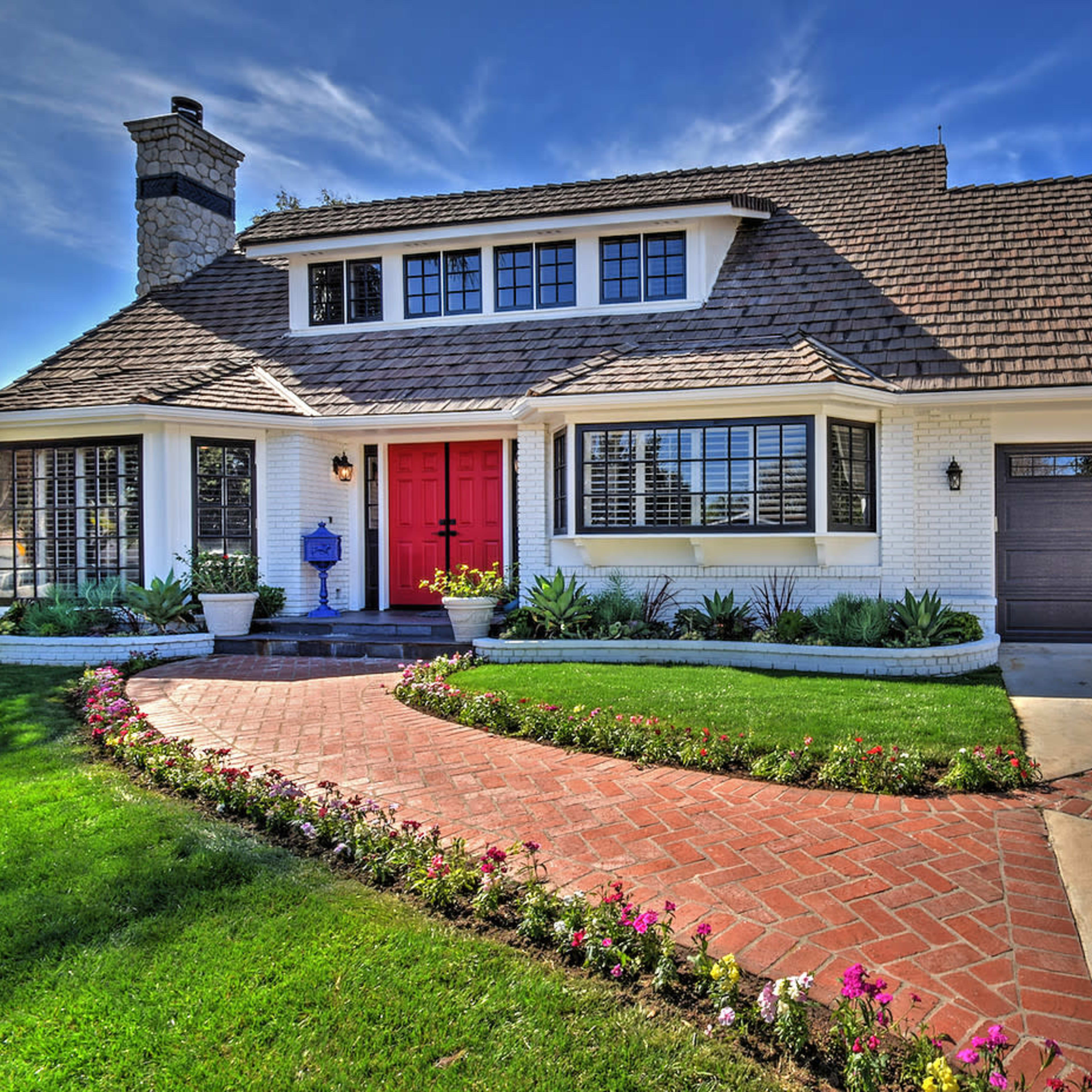 A two-story house with a red front door, a landscaped yard, and a brick pathway leading to the entrance.