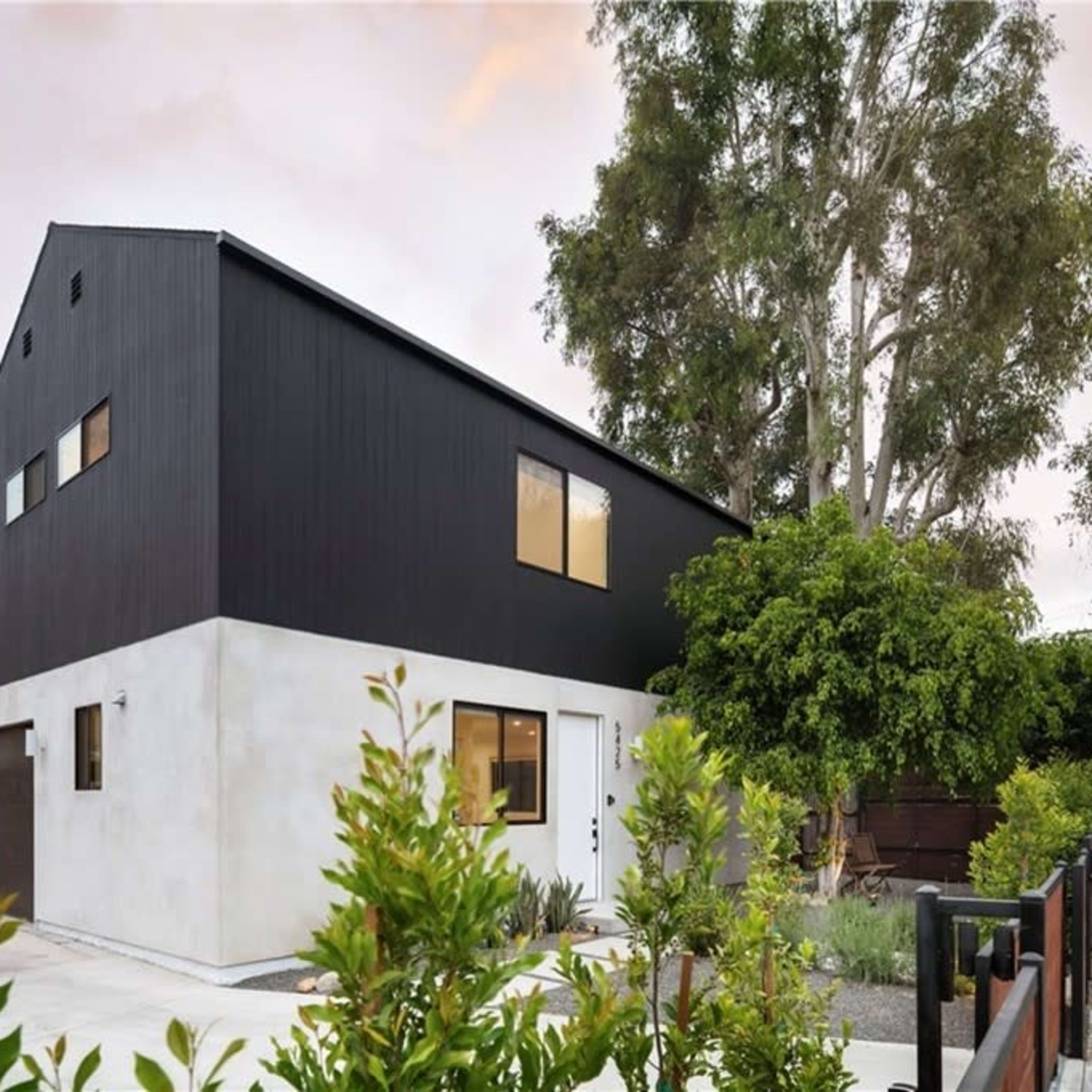 A modern two-story house with a black and white exterior, surrounded by greenery and a concrete driveway.