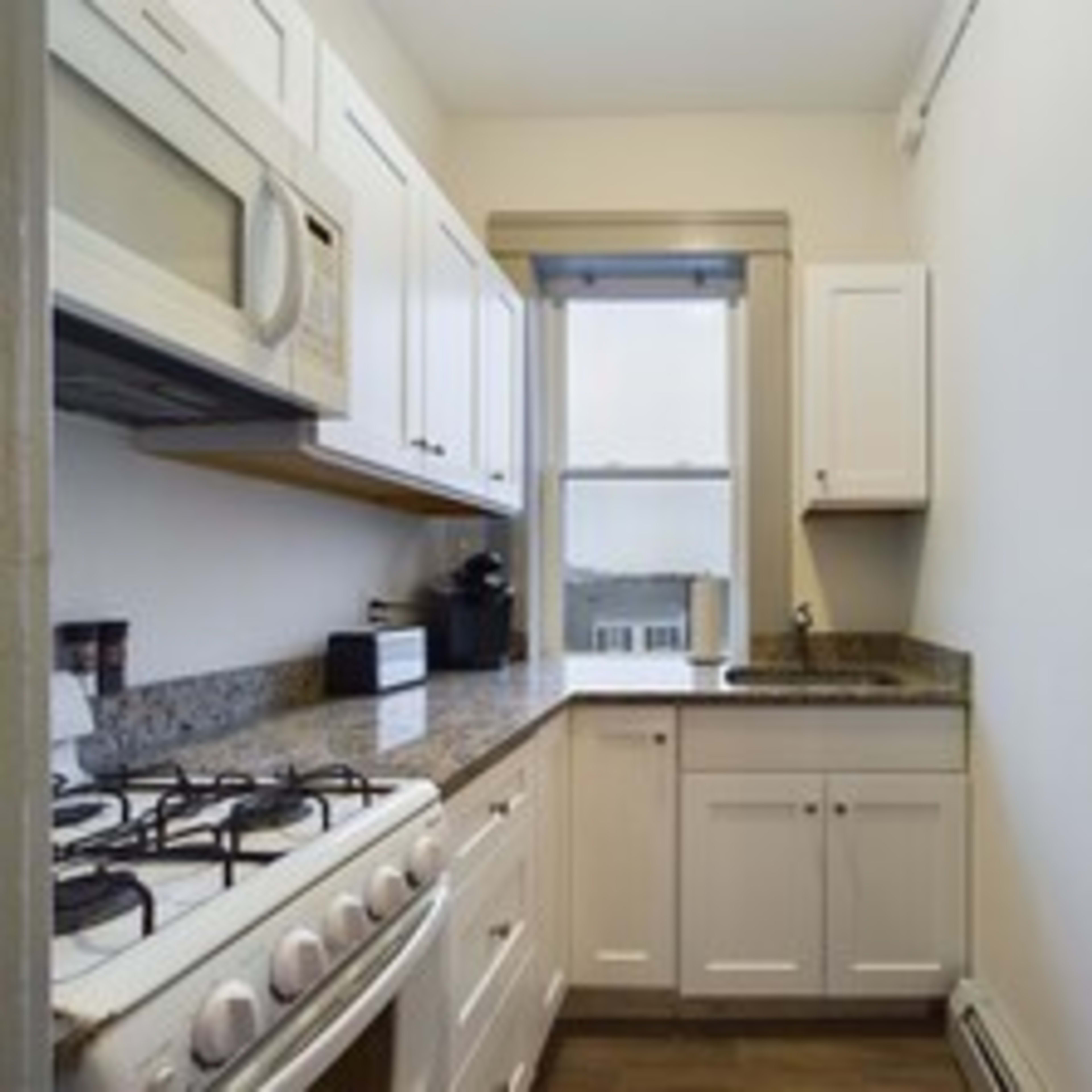A small kitchen with white cabinetry, a granite countertop, a gas stove, and a window.