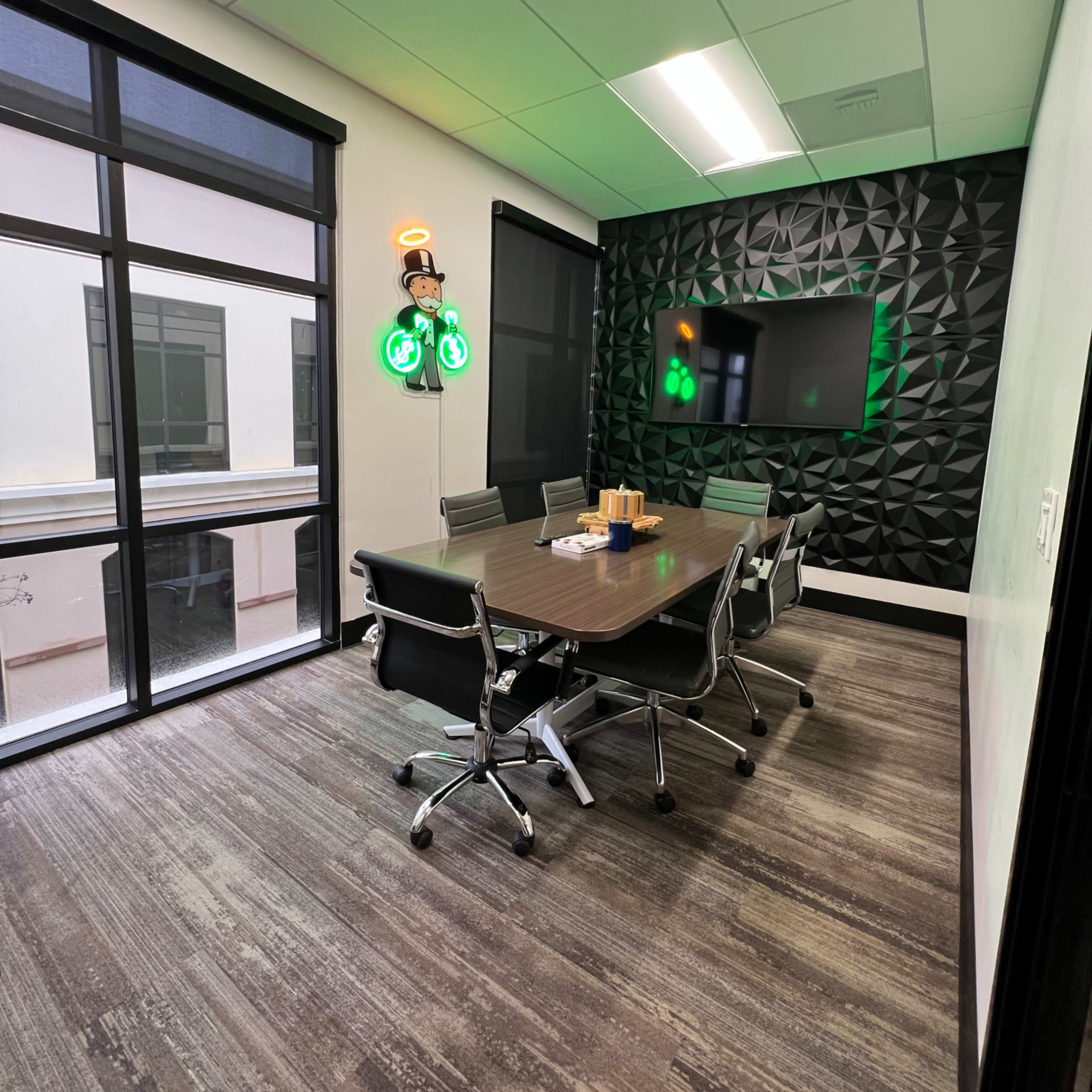 A modern conference room with a dark textured wall, a large screen, a rectangular table, and six ergonomic chairs.