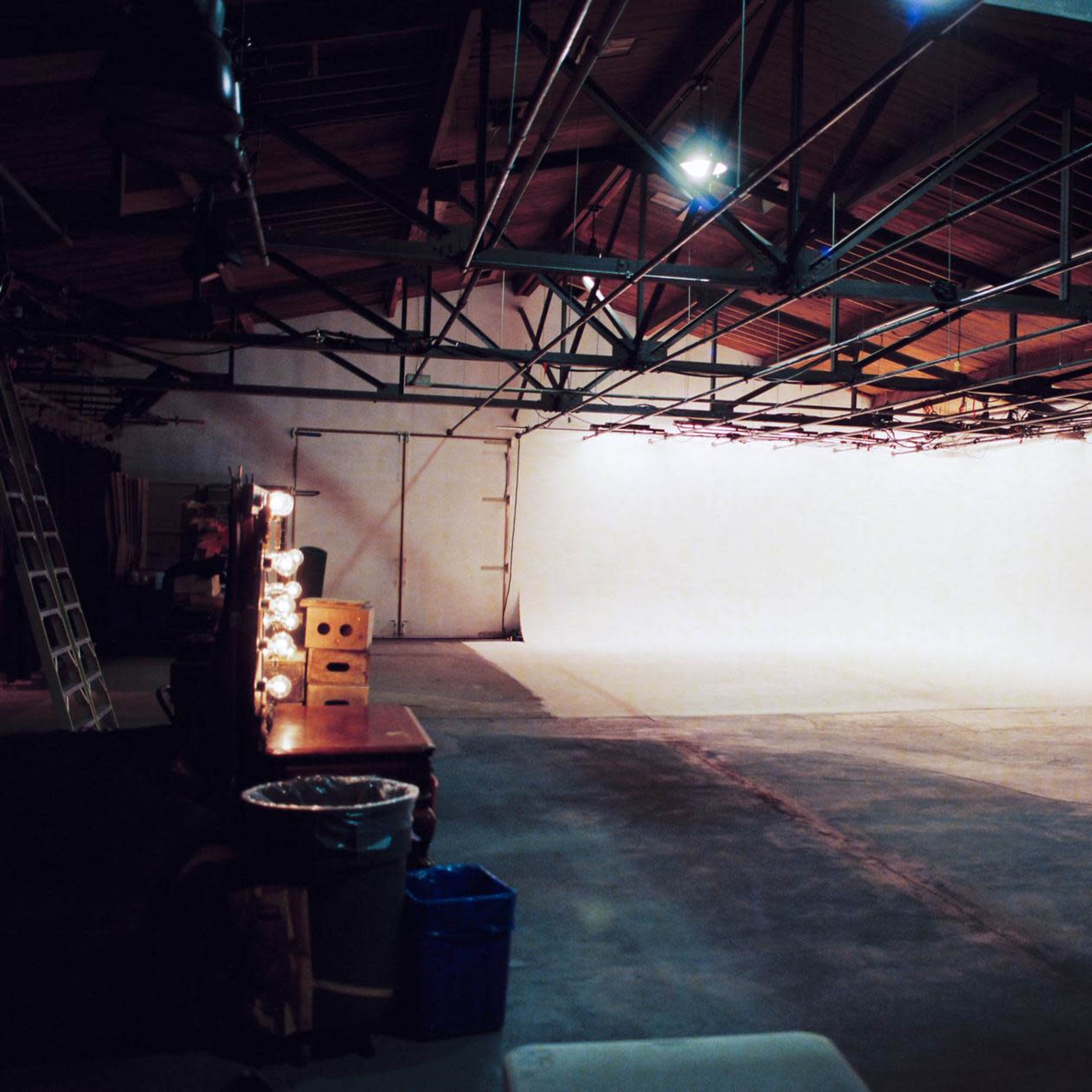 A large, empty studio space with a white backdrop and various equipment scattered along the edges.