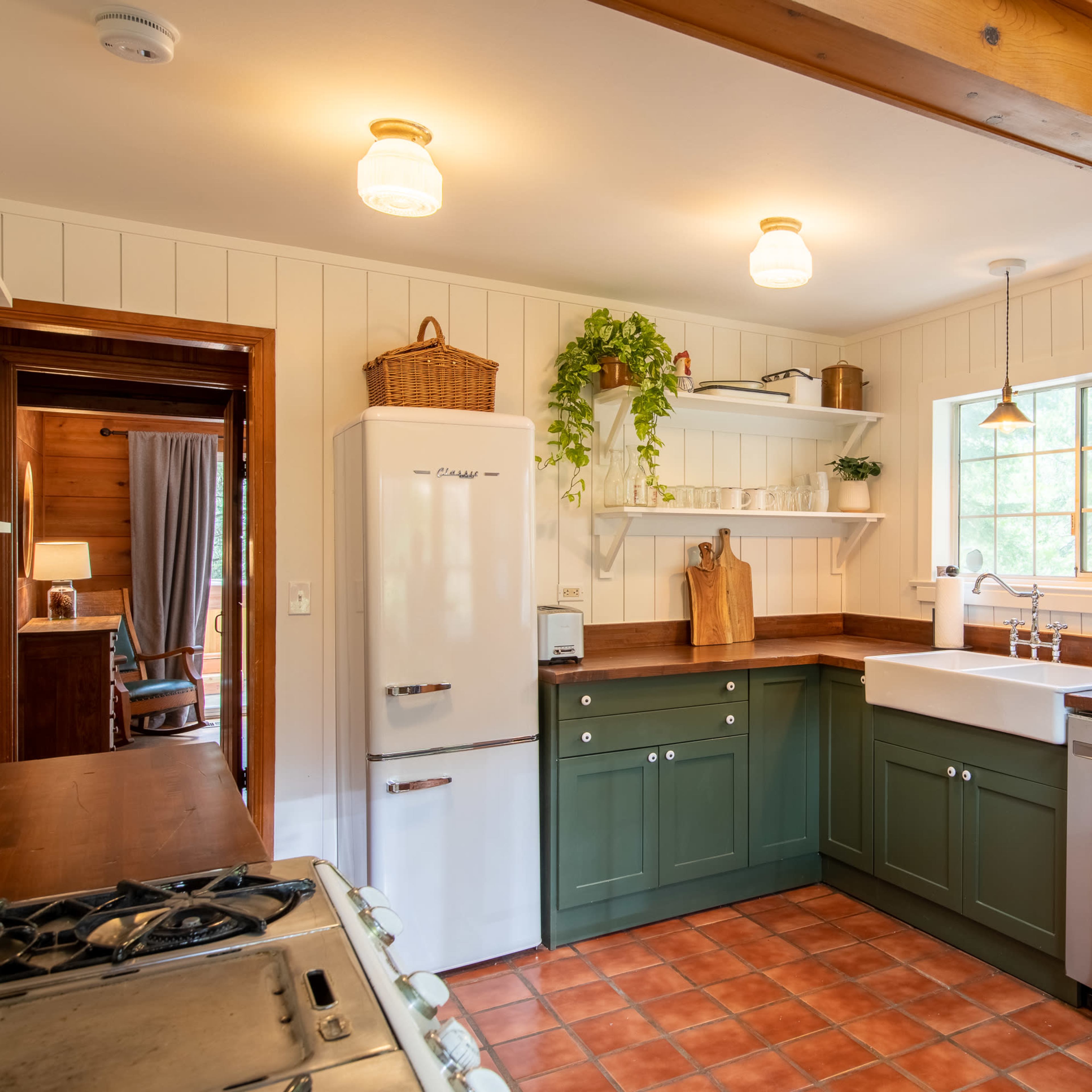 The kitchen features green cabinetry, a farmhouse sink, and wooden countertops, with a window providing natural light.