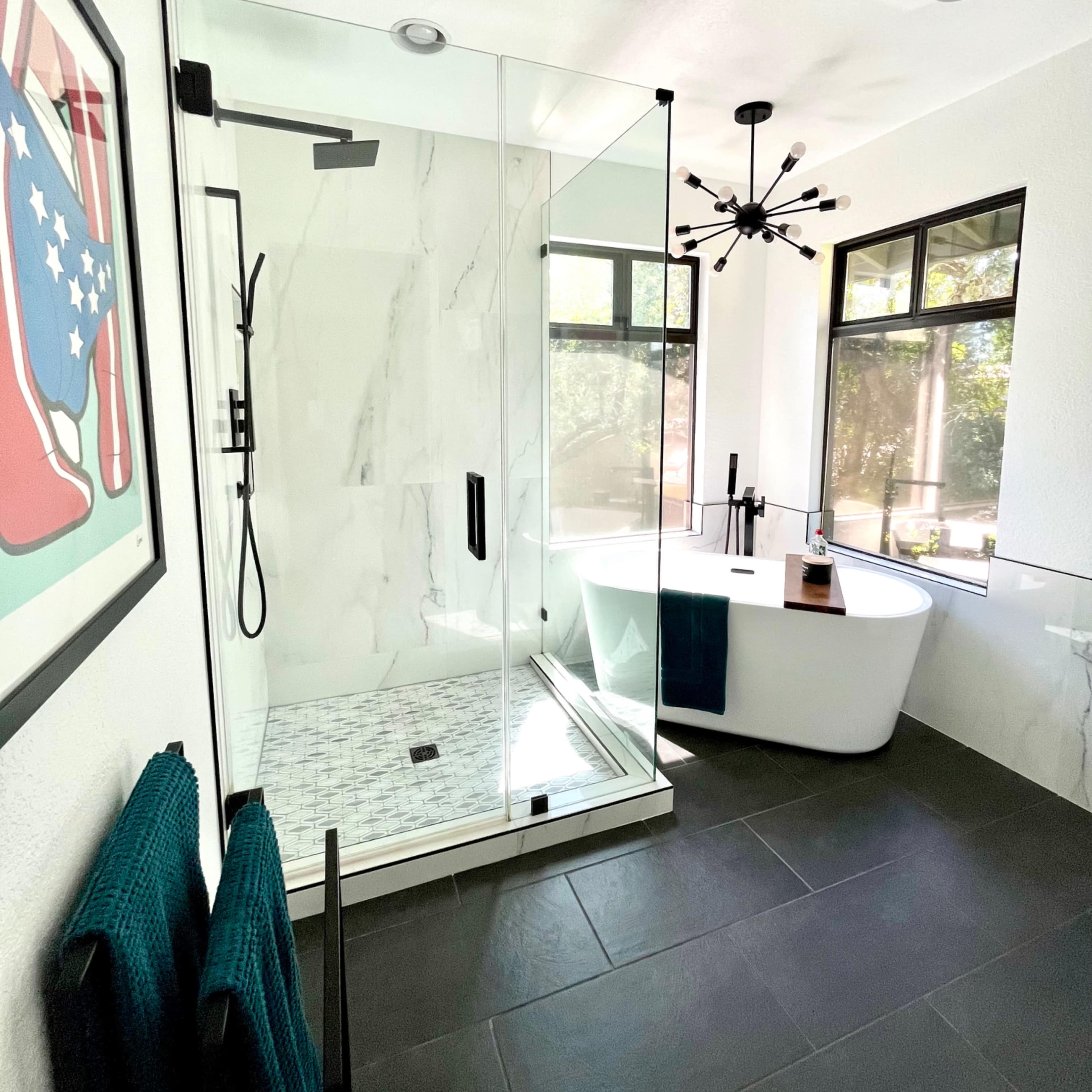 The bathroom features a glass-enclosed shower and a freestanding bathtub, with dark tile flooring and modern light fixtures.